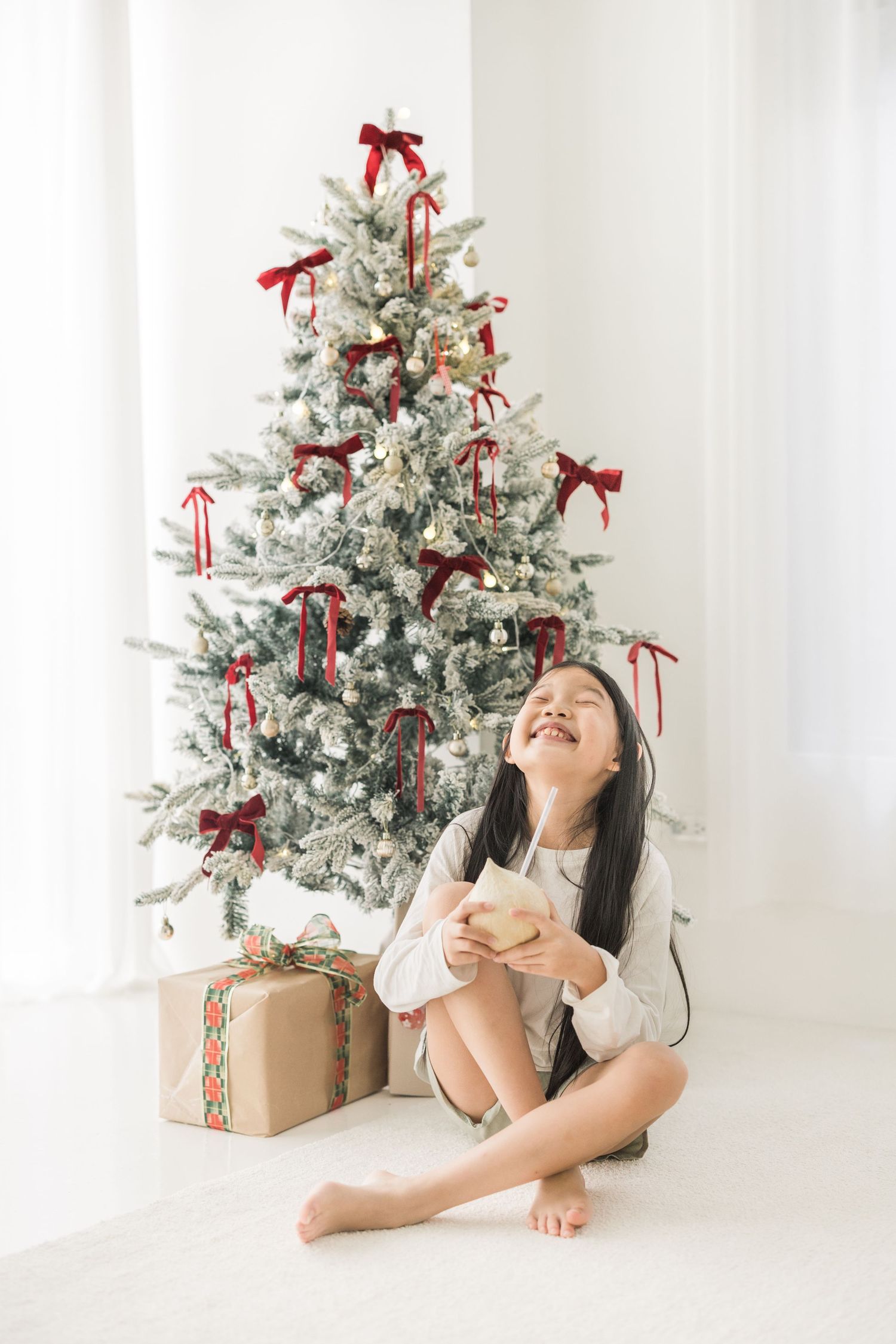 A festive white Christmas scene with a decorated tree, red bows, and wrapped presents on a bright background.