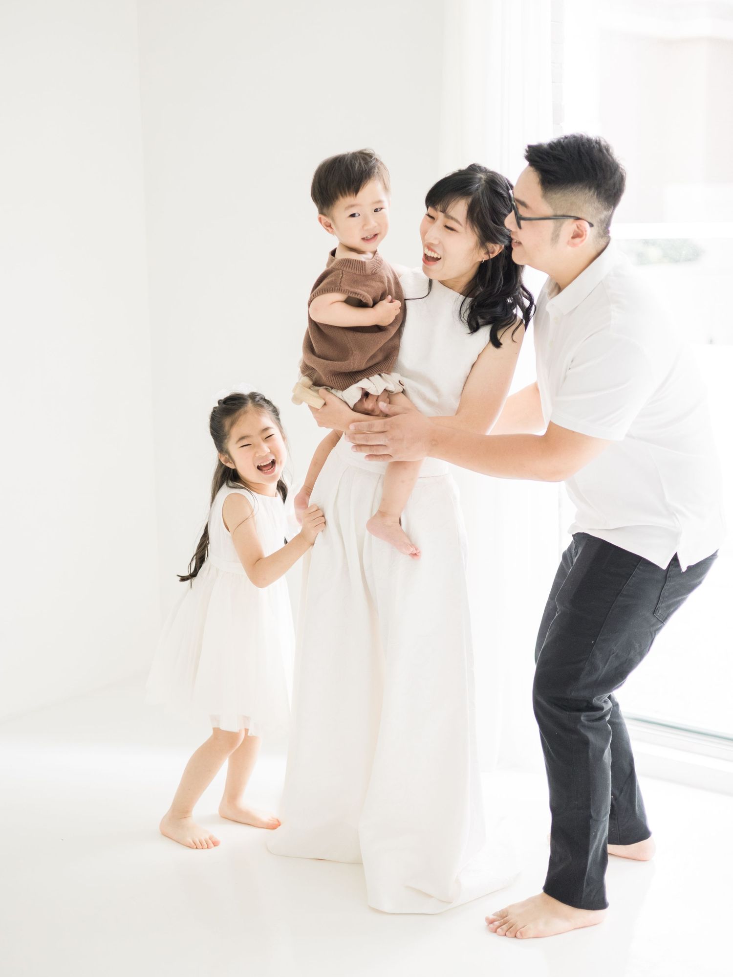 A loving family sharing playful moments together in a bright white studio setting.