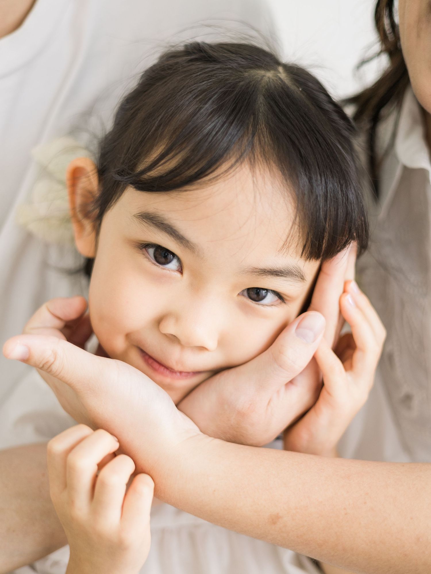 A close up portrait in soft lighting with hands framing the subject's face.