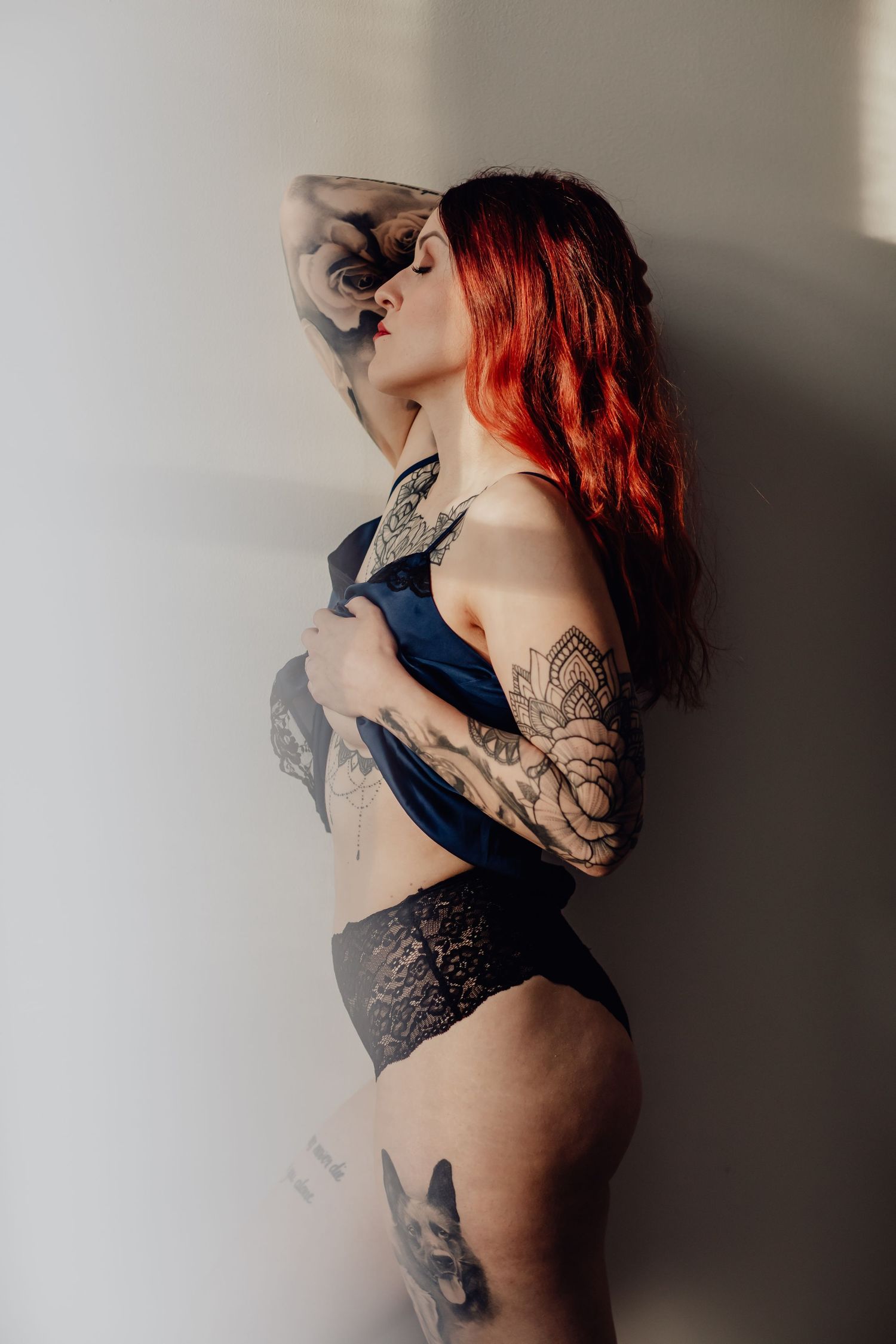 Tatuoitu nainen nojaa seinään boudoir-kuvauksessa