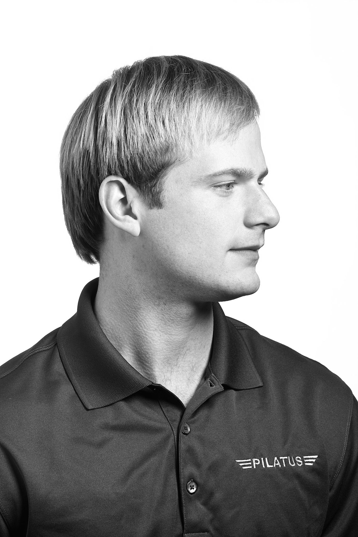 Black and white side profile portrait of a man with short hair wearing a collared polo shirt with a Pilatus logo.