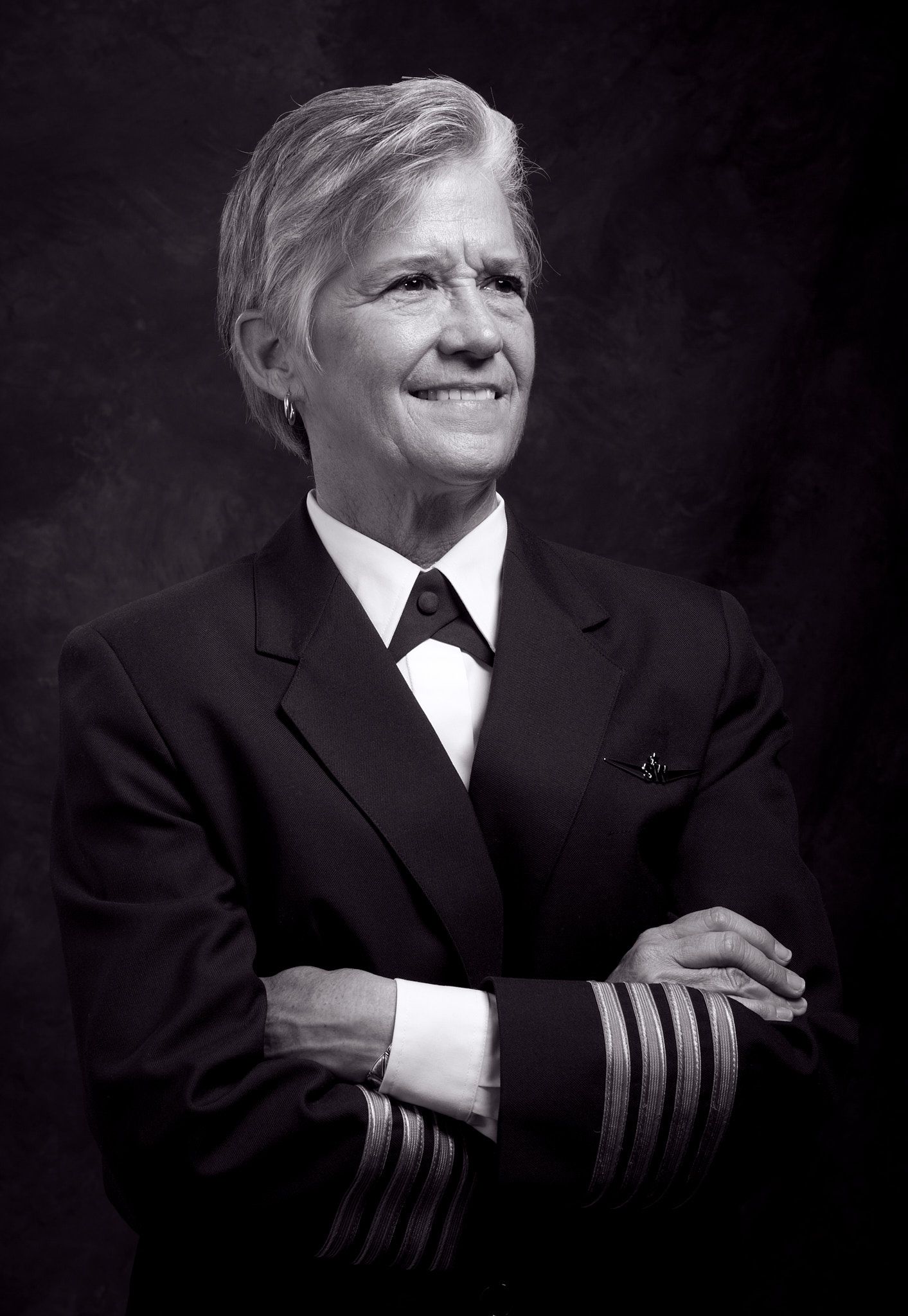 Black and white portrait of a smiling female airline captain in a uniform with four sleeve stripes and arms crossed.