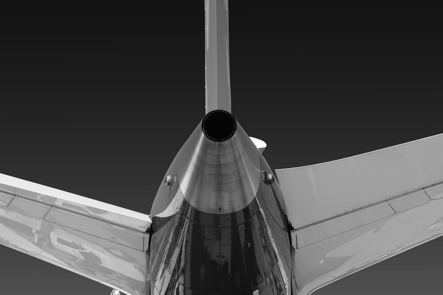 Black and white rear view of an airplane tail with engine exhaust and swept horizontal stabilizers against a dark sky.