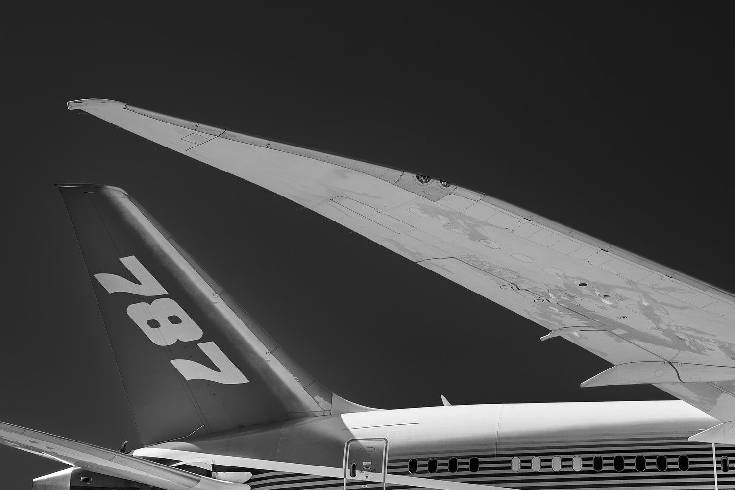 Black and white photo of a Boeing 787 Dreamliner showing the curved wingtip and tail fin marked 787 against a dark sky.