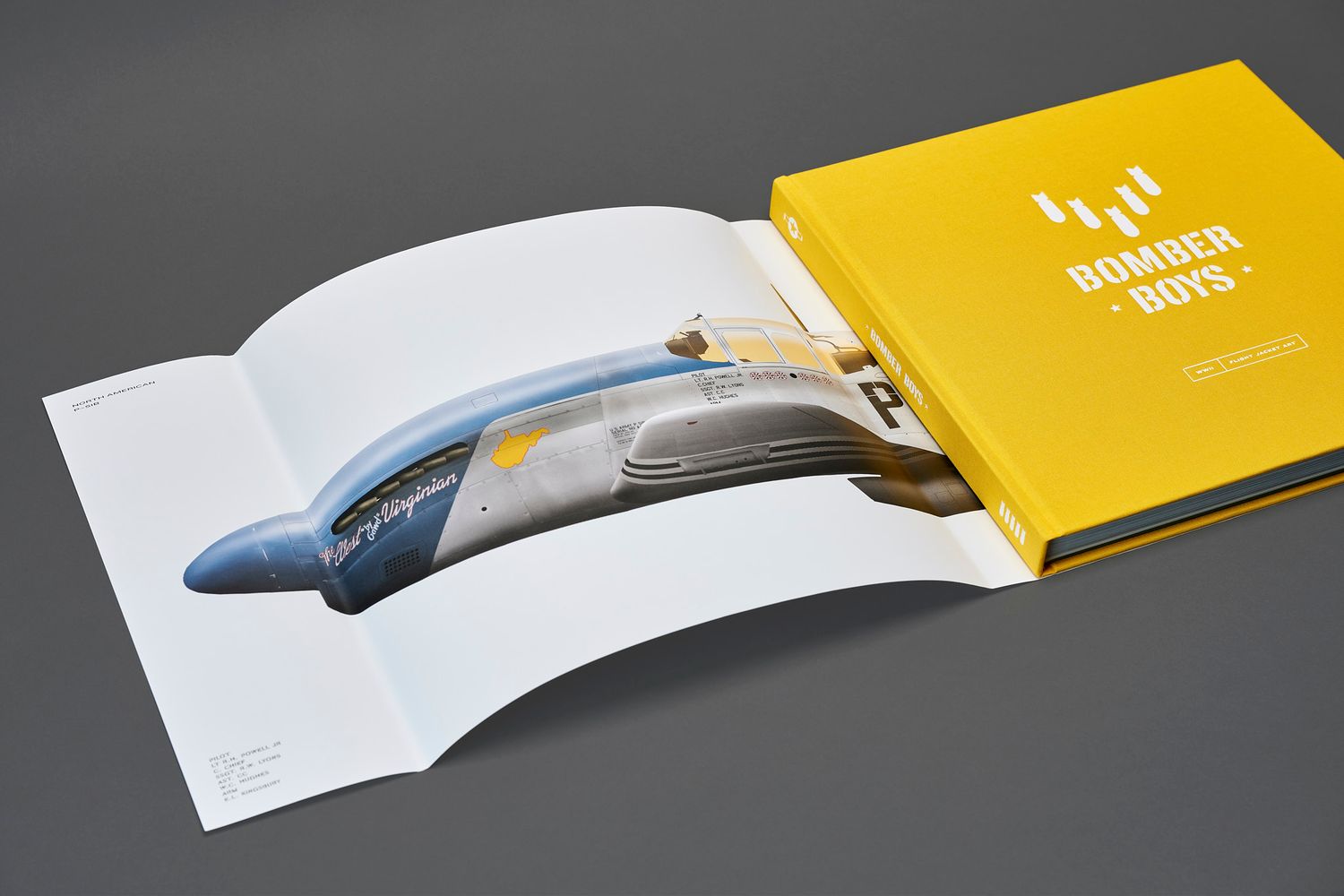 Yellow Bomber Boys hardcover book lying next to an open page showing a blue and silver vintage aircraft nose illustration.