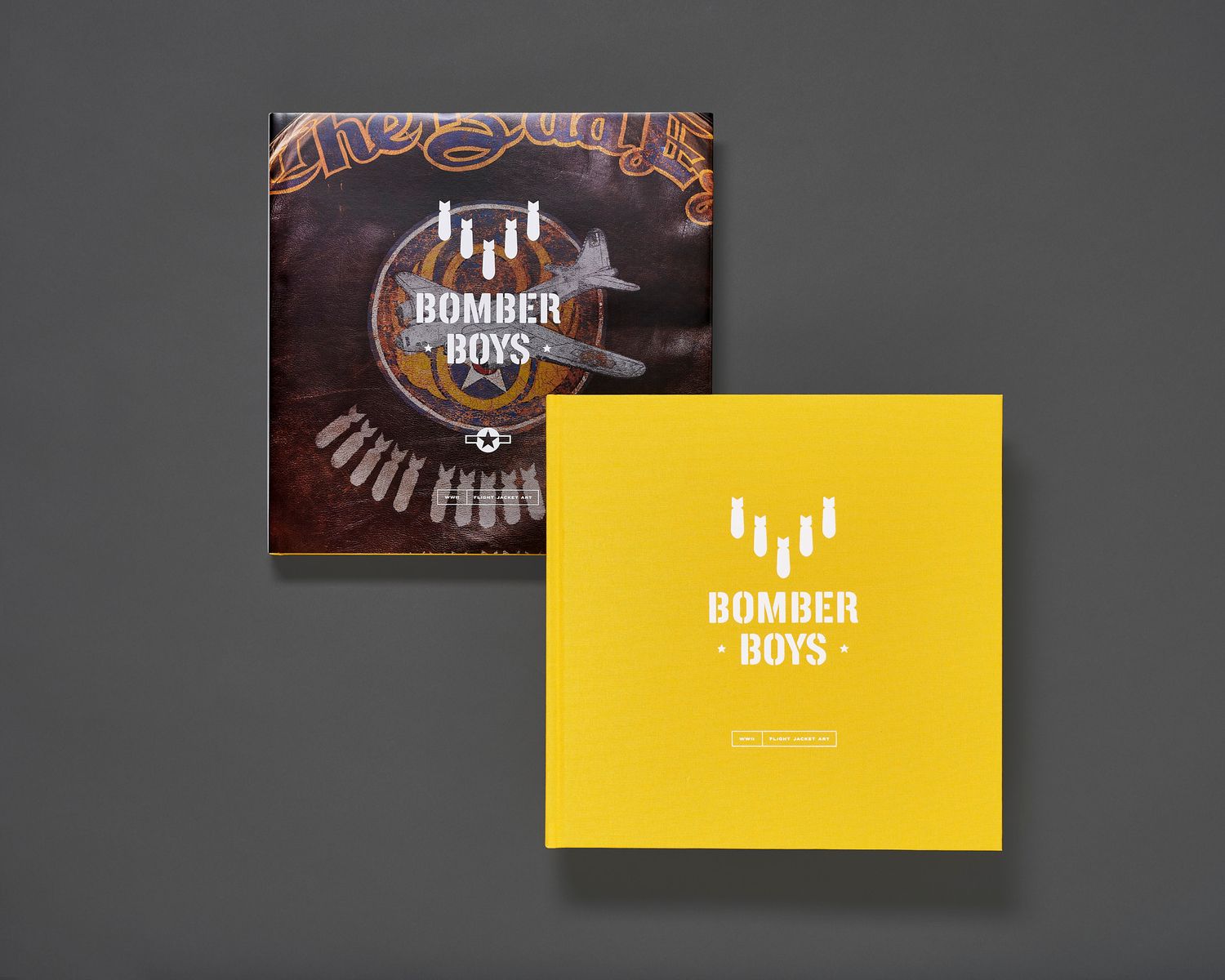 Two Bomber Boys books on a gray surface, one with a brown leather jacket art cover and one with a bright yellow cover and white logo.