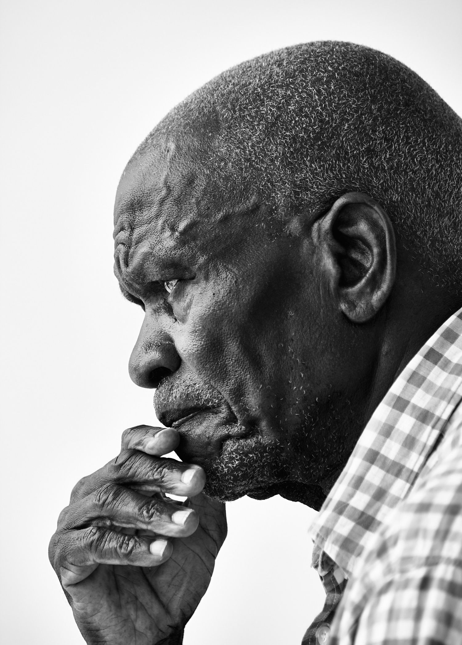 Black and white profile portrait of an elderly man in a checkered shirt resting his chin on his hand in quiet, thoughtful contemplation.