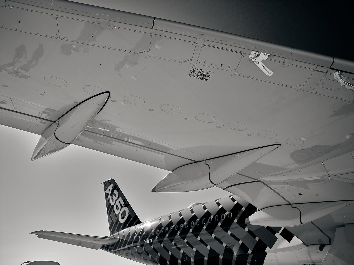 Black and white view of an airliner wing with curved winglets and an A350 tail fin with a checkered carbon pattern.