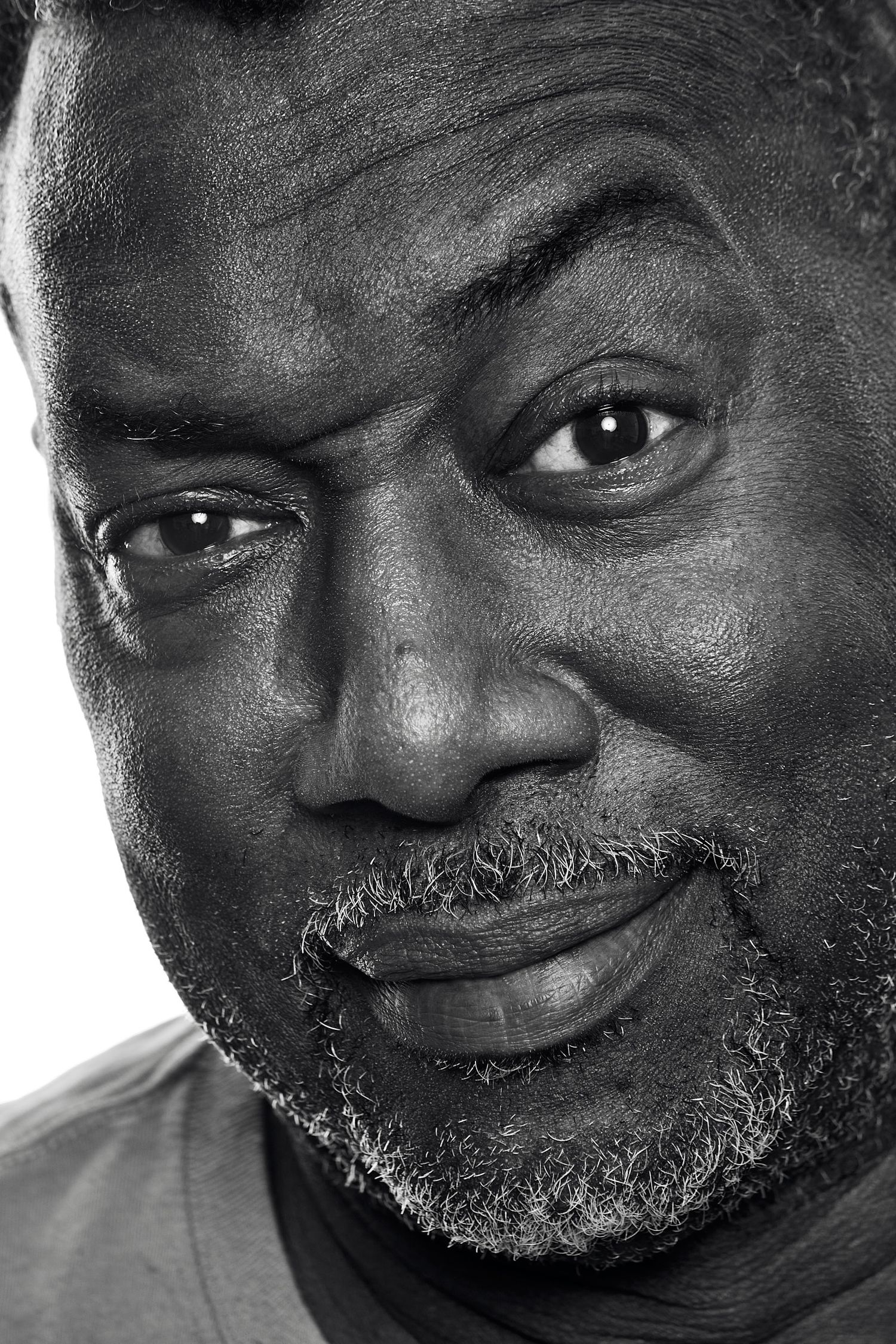 Black and white close-up portrait of a middle-aged man with a salt-and-pepper beard, furrowed brow, and a warm, knowing expression.