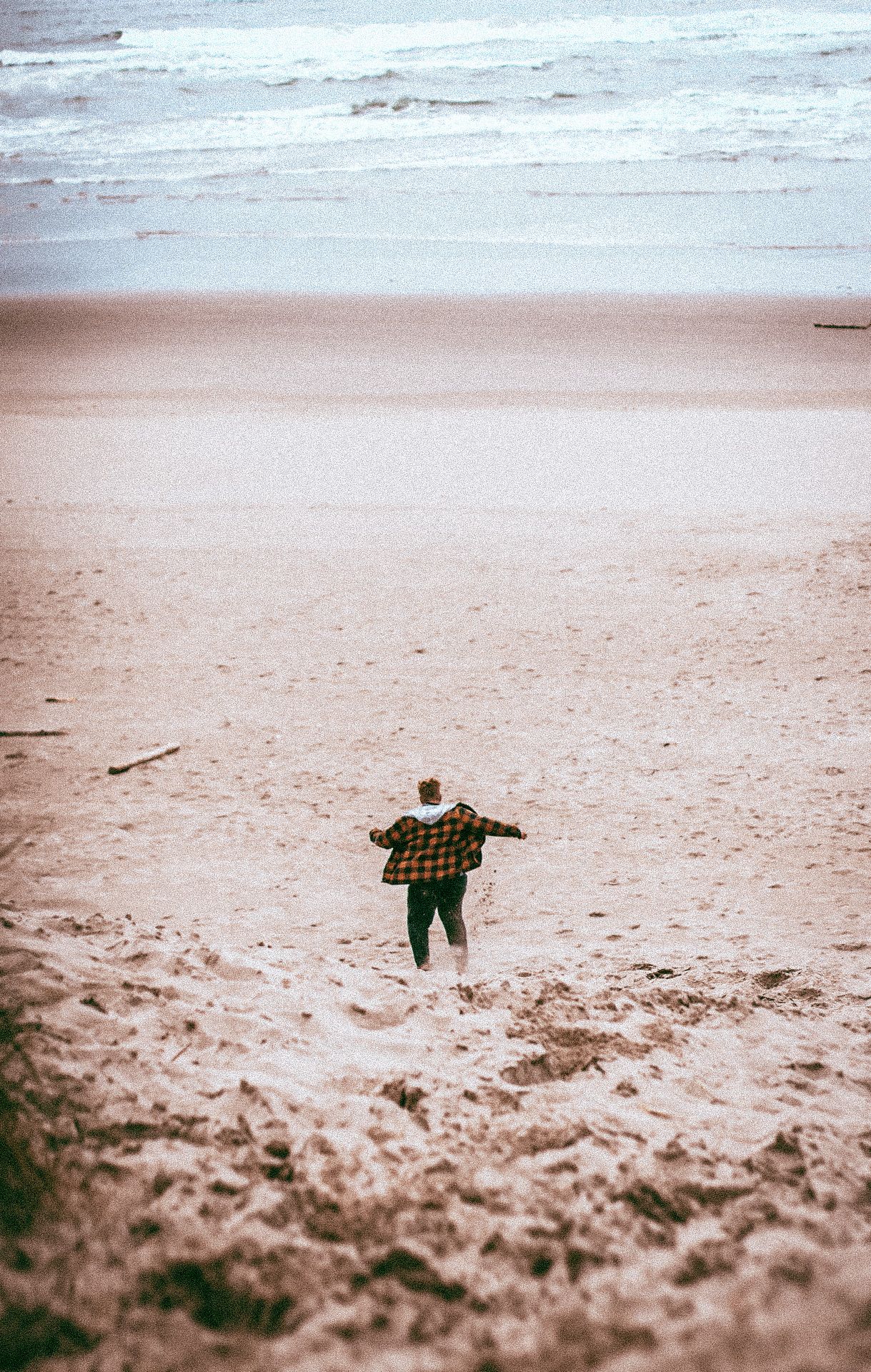 Man in orange plaid jacket and black jeans running to the ocean at Oregon Sand Dunes State Park.