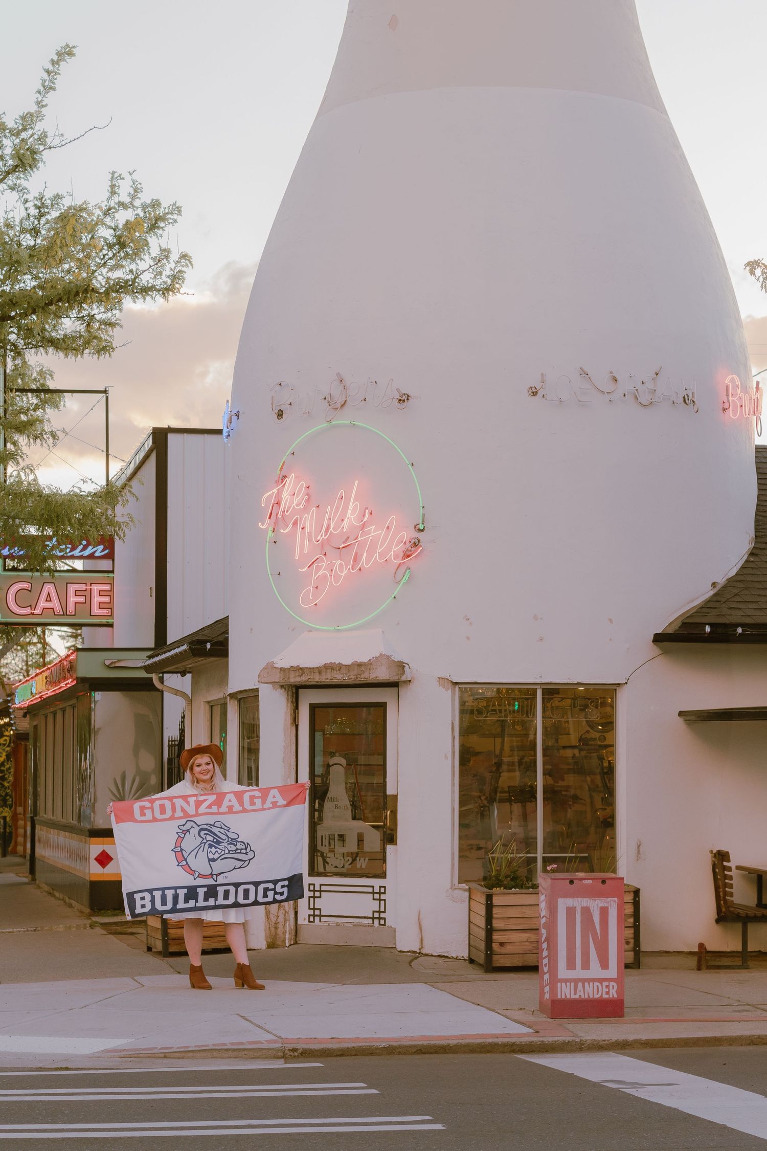 Spokane college graduate posing with a Gonzaga Bulldogs flag in front of The Milk Bottle in the Garland, North Hill Neighborhood in East WA.