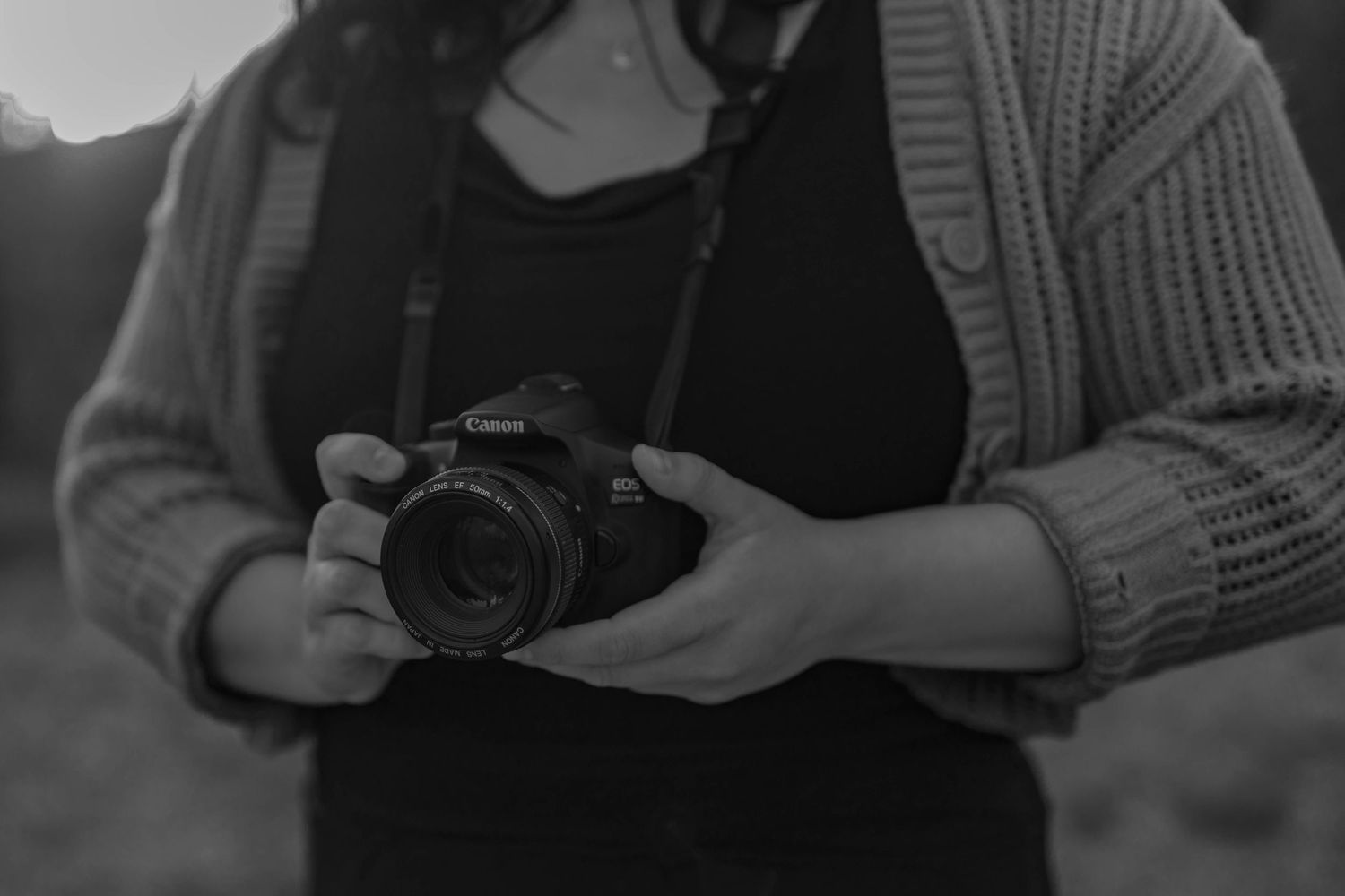 Canon T6 camera being held by woman in black attire and a cardigan.