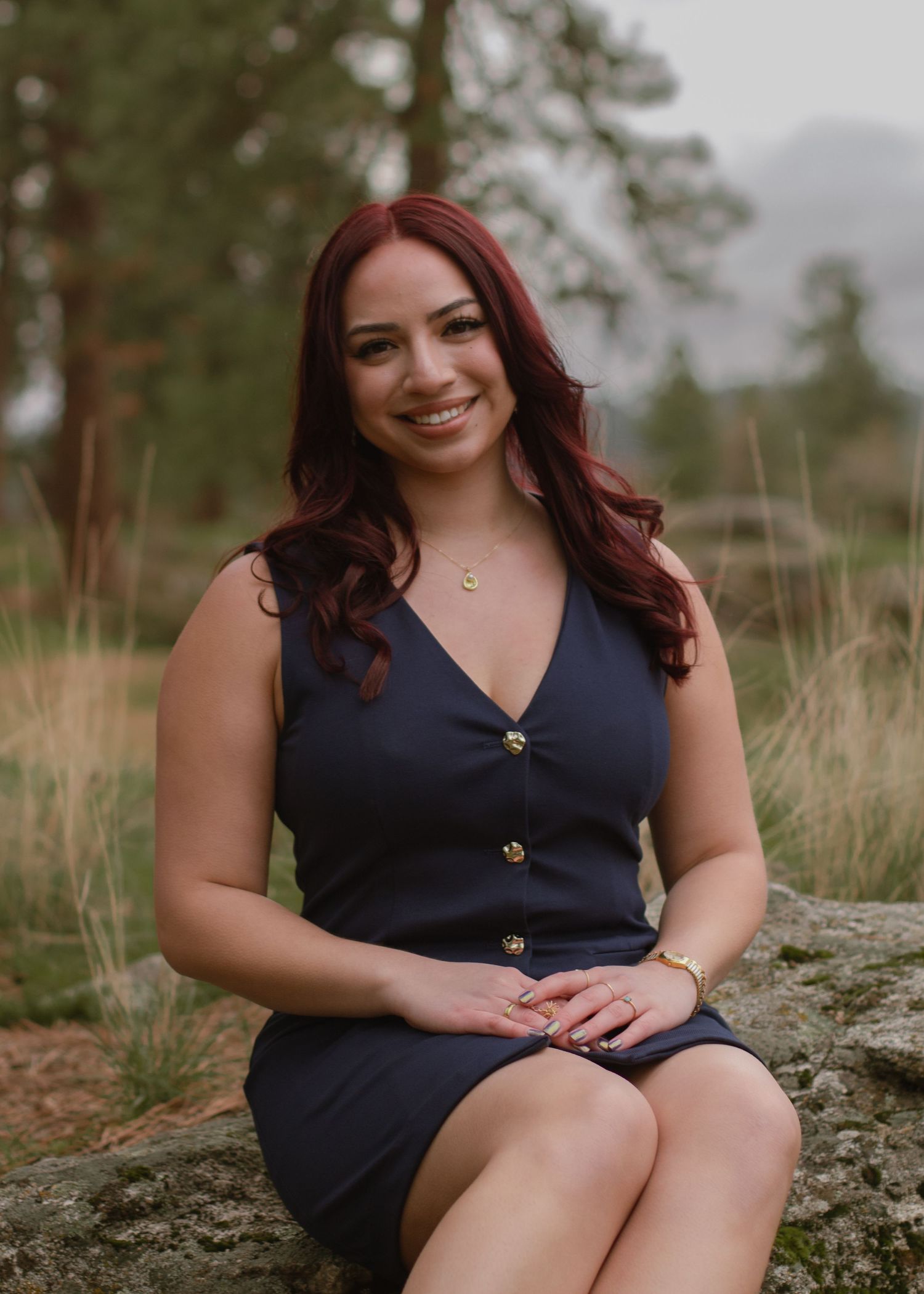 Woman with cherry red hair in a deep blue dress posing with hands placed in lap sitting on a rock at Mirabeau Park.