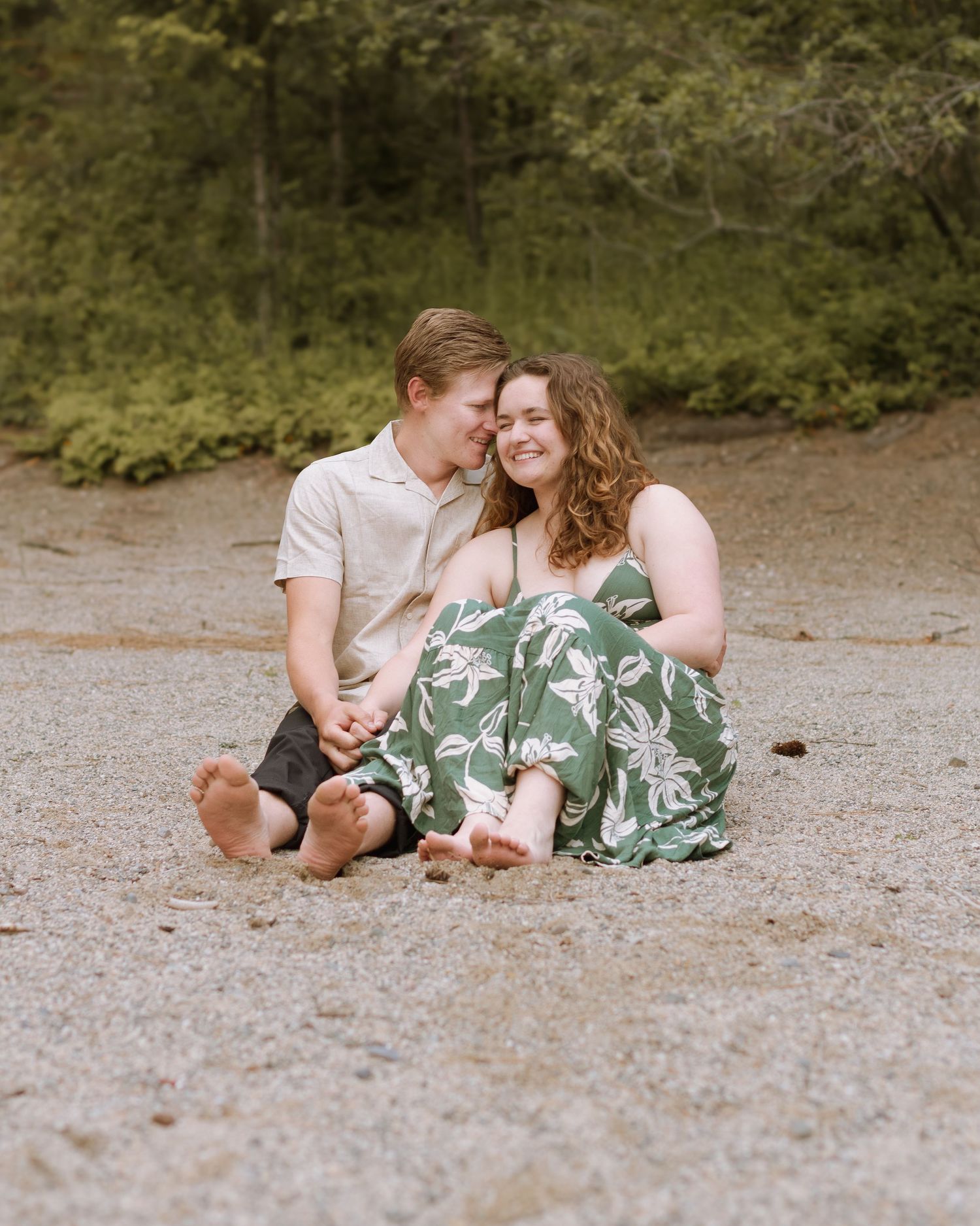 Couple cuddling up close at the beach by the lake for engagement session at Farragut State Park in Athol, Idaho.