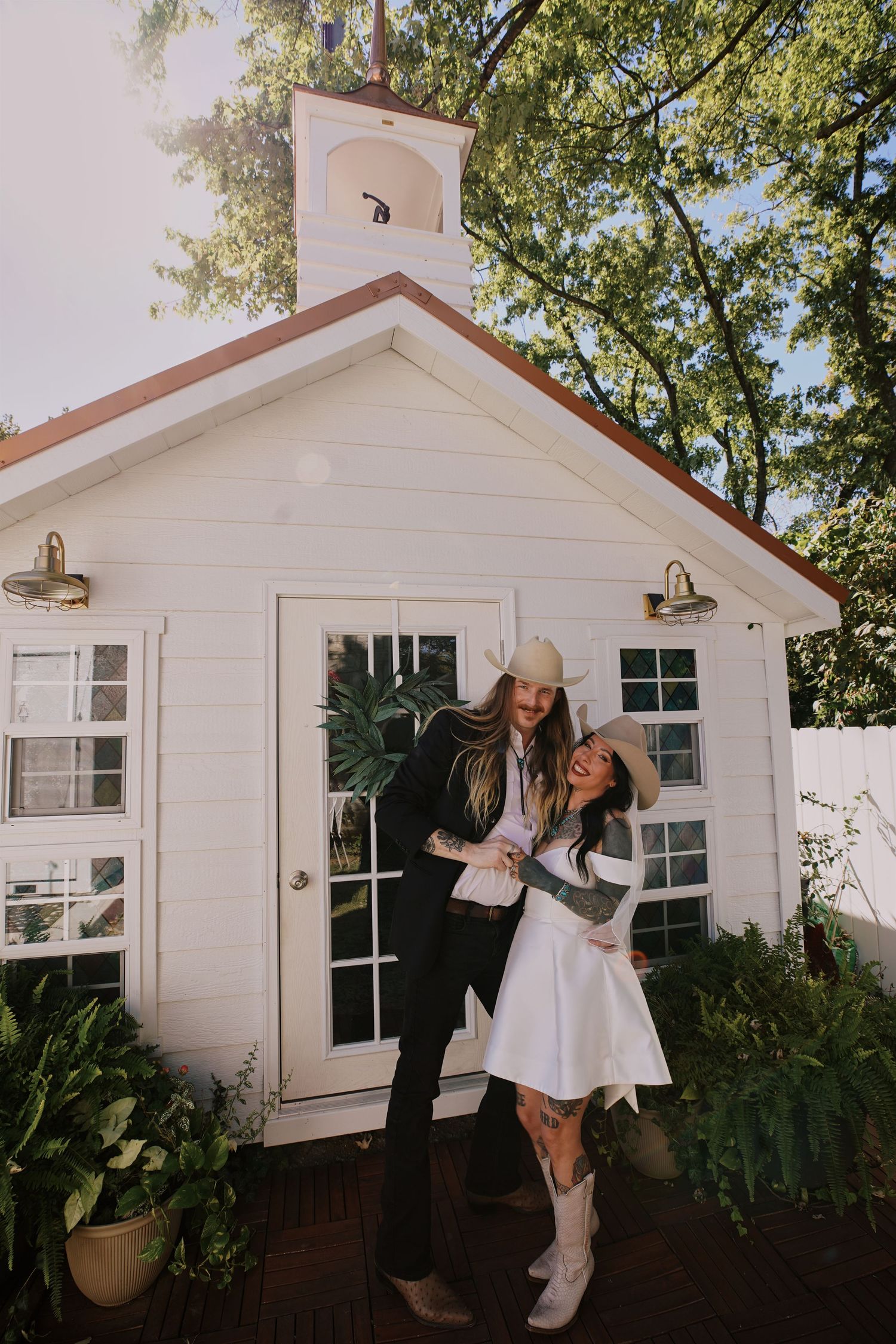 A charming white chapel-style building with French doors and rustic barn lights creates a cozy outdoor setting.