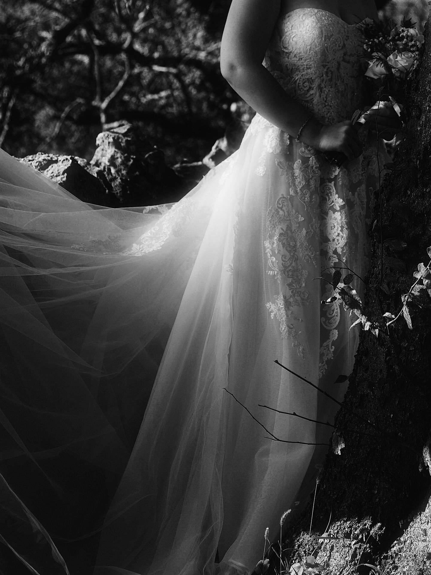 A flowing white wedding dress billows dramatically in black and white as it catches the wind outdoors.
