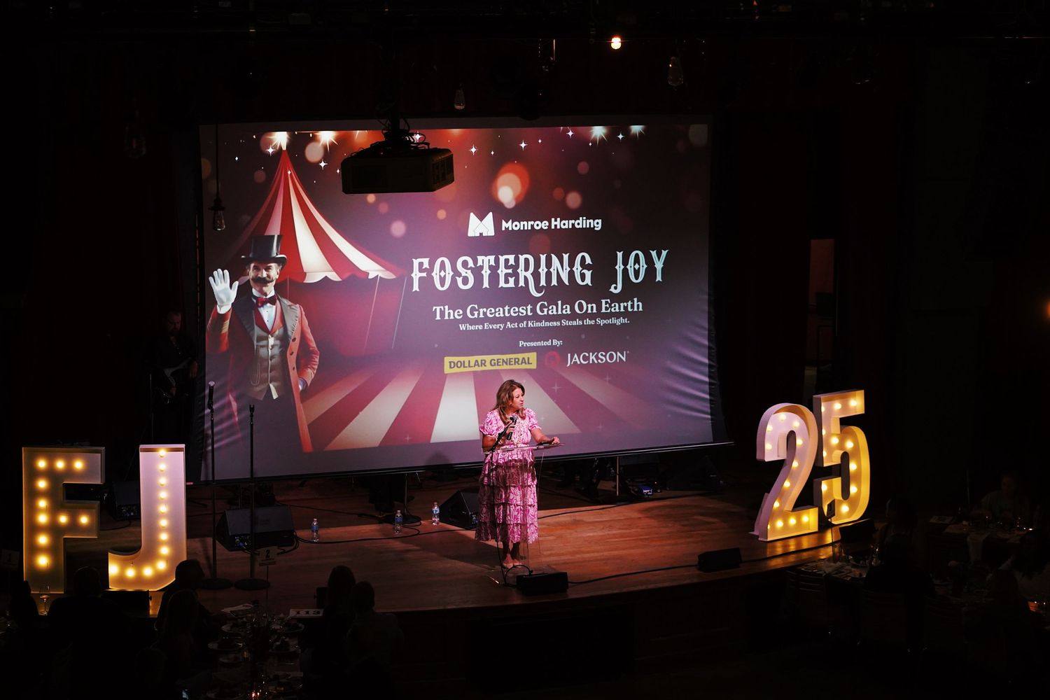 Dark stage setup with theatrical lighting and performance screen displaying 'Fostering Joy'.