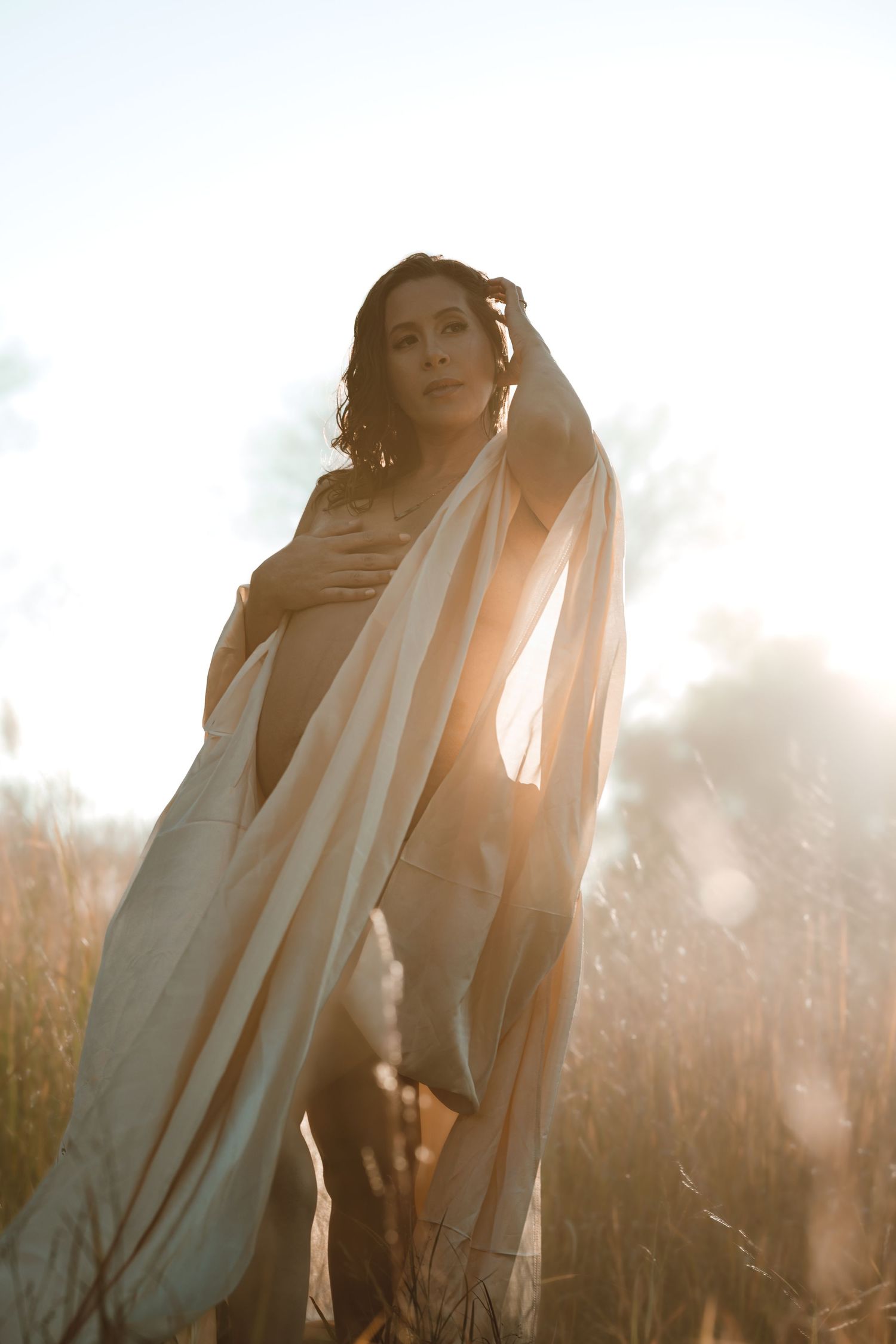 A pregnant woman's silhouette in dreamy sunlight create an ethereal romantic atmosphere during golden hour for maternity photoshoot.