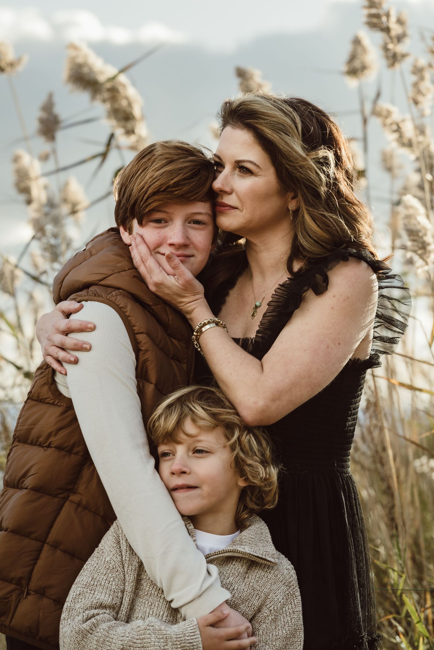 A family shares tender moments together while standing in tall grass during golden hour.