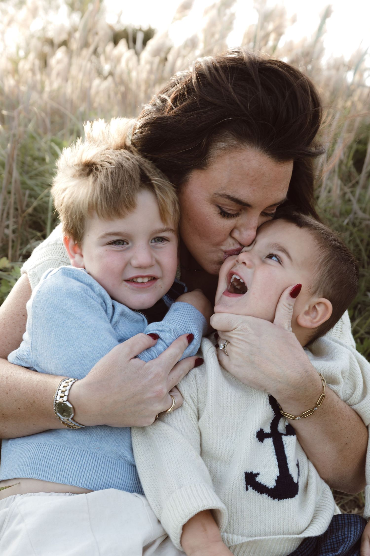 A mom and her two boys showing playful affection and hugging between in white and blue sweaters.
