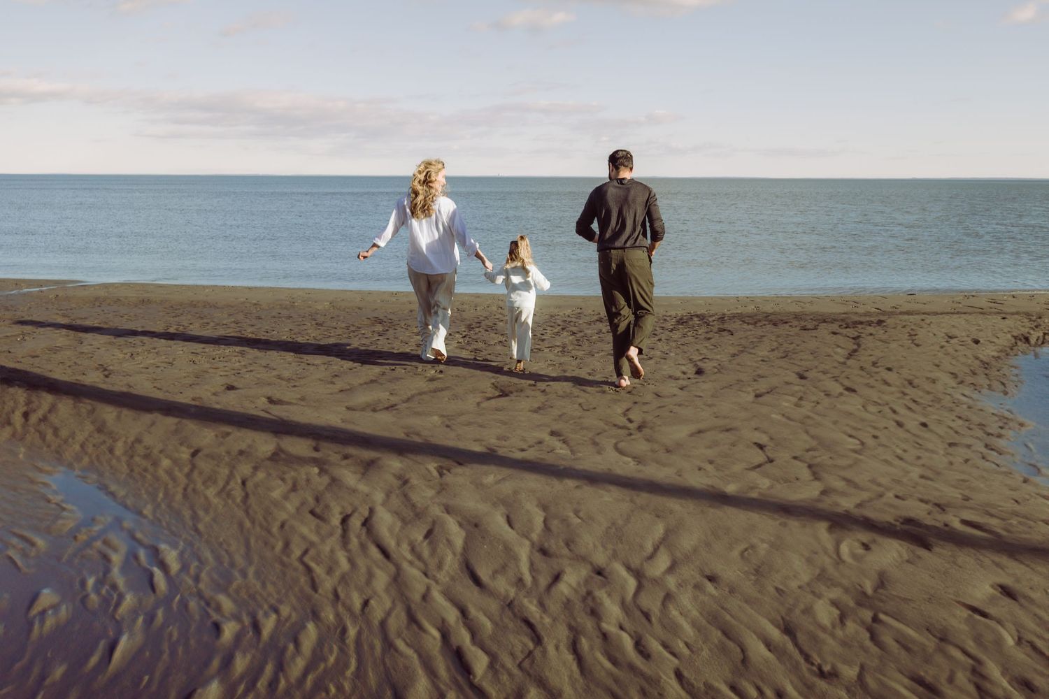 Family of three  jog together along a sandy beach beside the ocean at sunset in Westport during maternity photoshoot