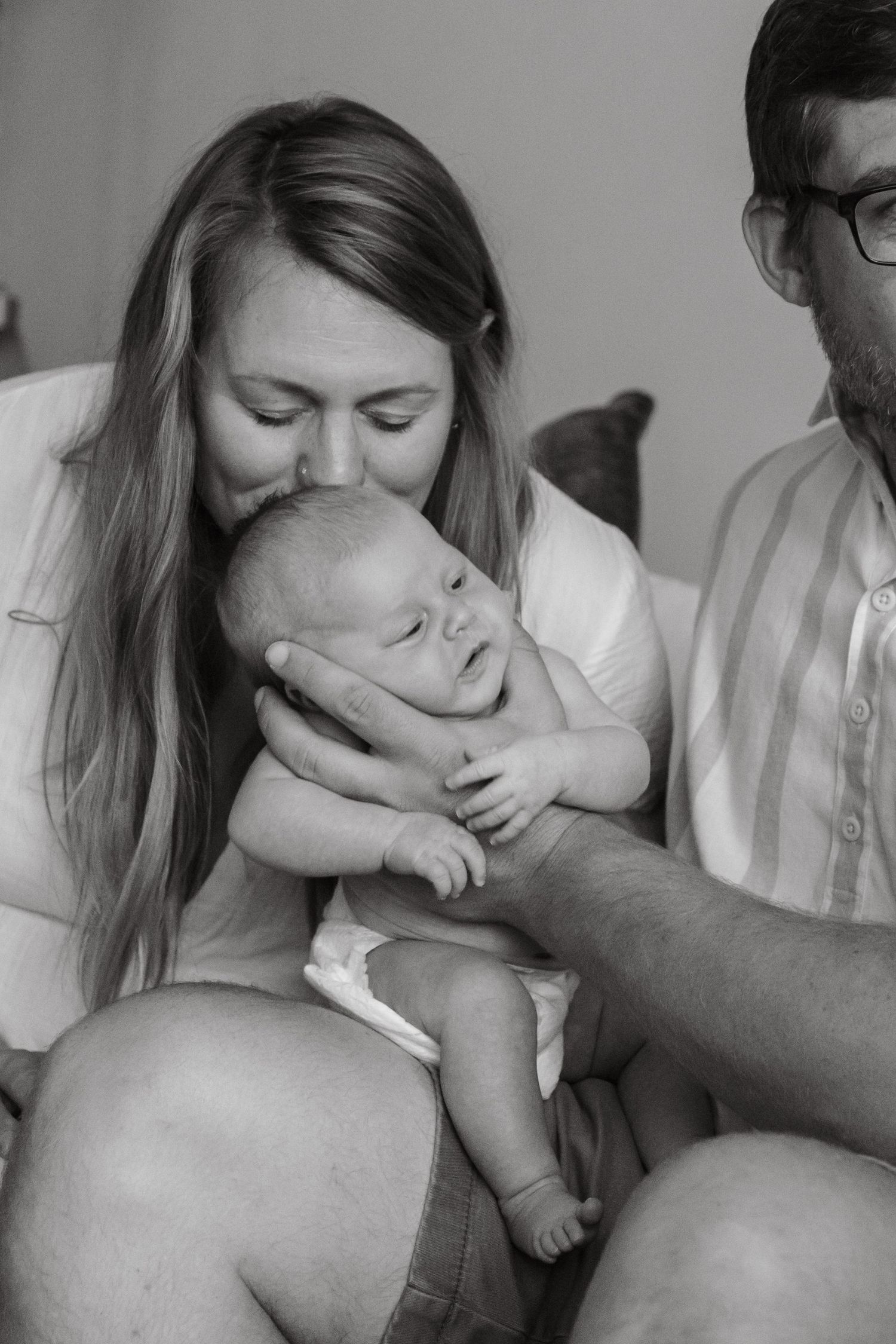 A tender black and white portrait of parents sharing an intimate moment with their sleeping newborn baby.