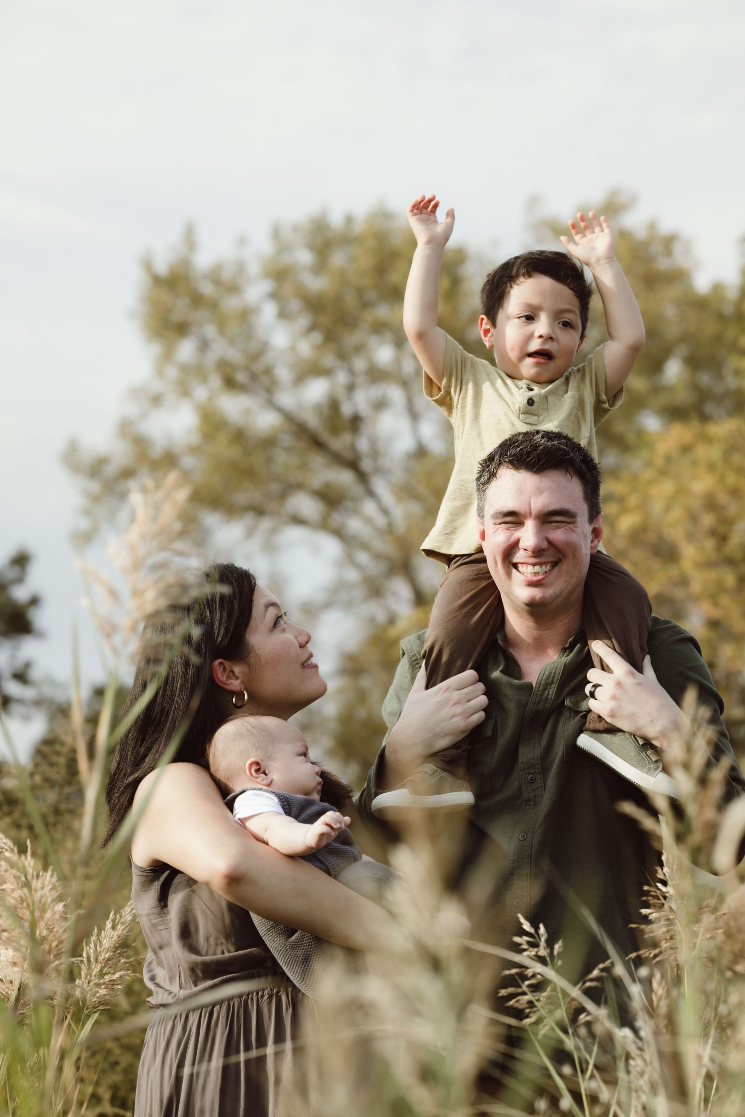A joyful family plays together in a field of tall grass during a warm autumn day on the beach for a summer family photoshoot.
