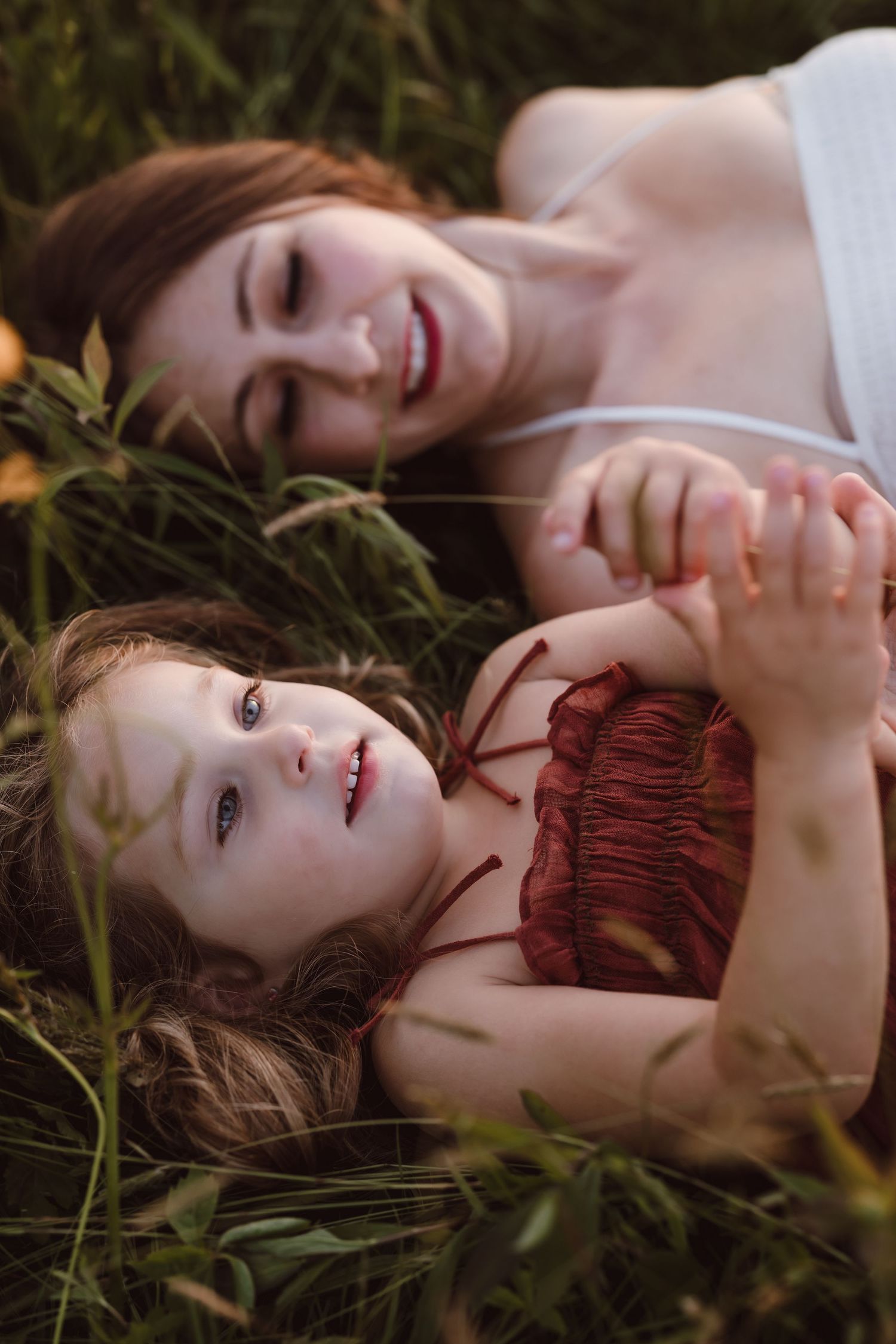 A series of dreamy portraits showing someone lying in grass wearing a red dress in soft natural lighting.