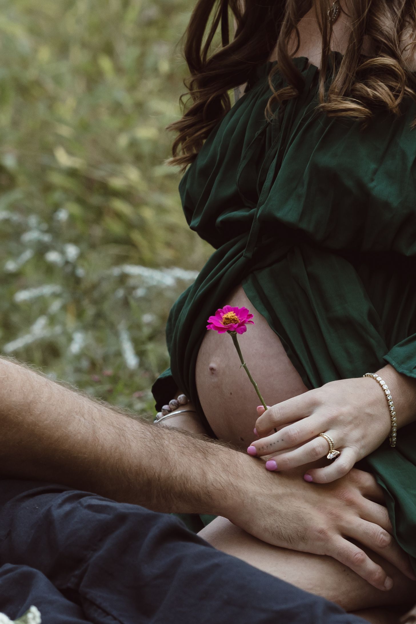 A series of hands holding a small pink flower against a pregnant belly during a photo session for their baby girl.