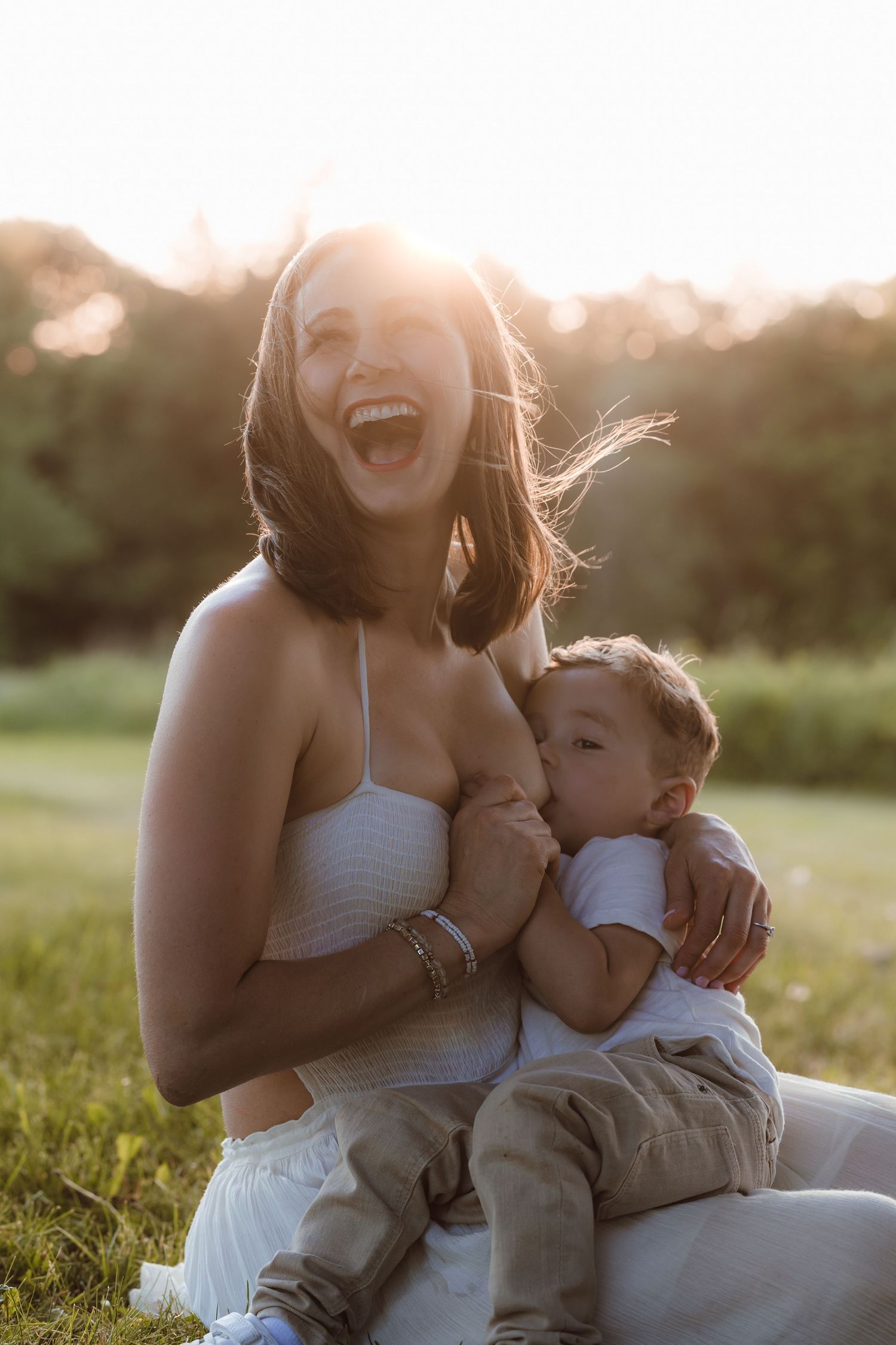 A mother celebrating her last breastfeeding milestone with her toddler son in a green grassy meadow in late spring for photoshoot in CT.