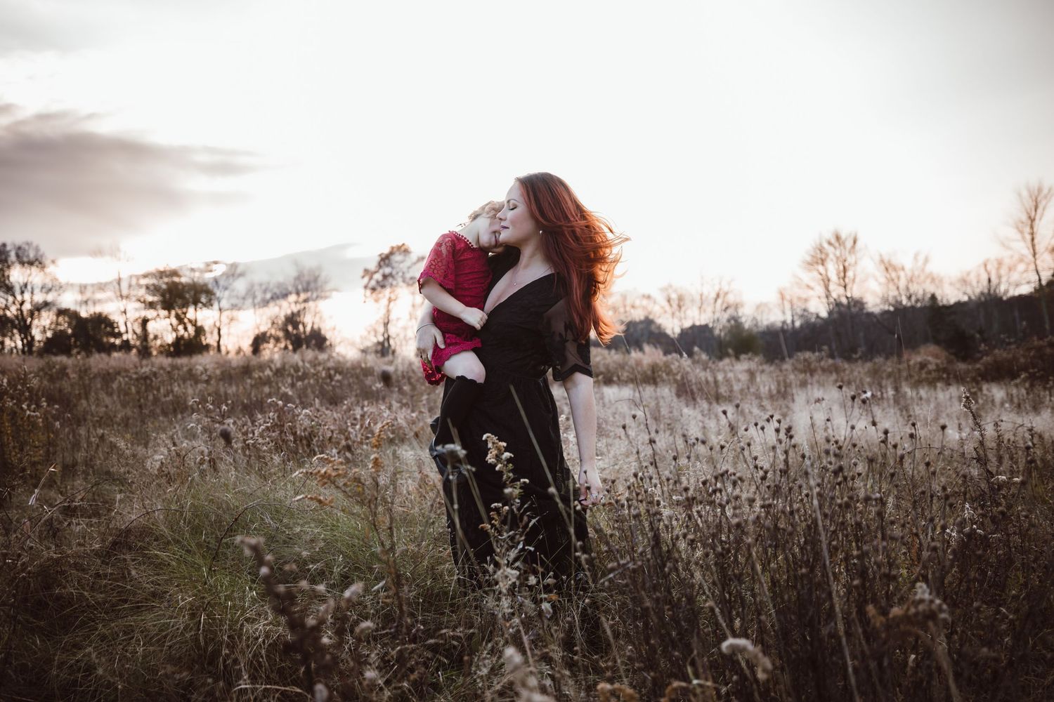 A mother and daughter embraces in a misty field of tall grass during sunset for family photoshoot in Newtown Connecticut.