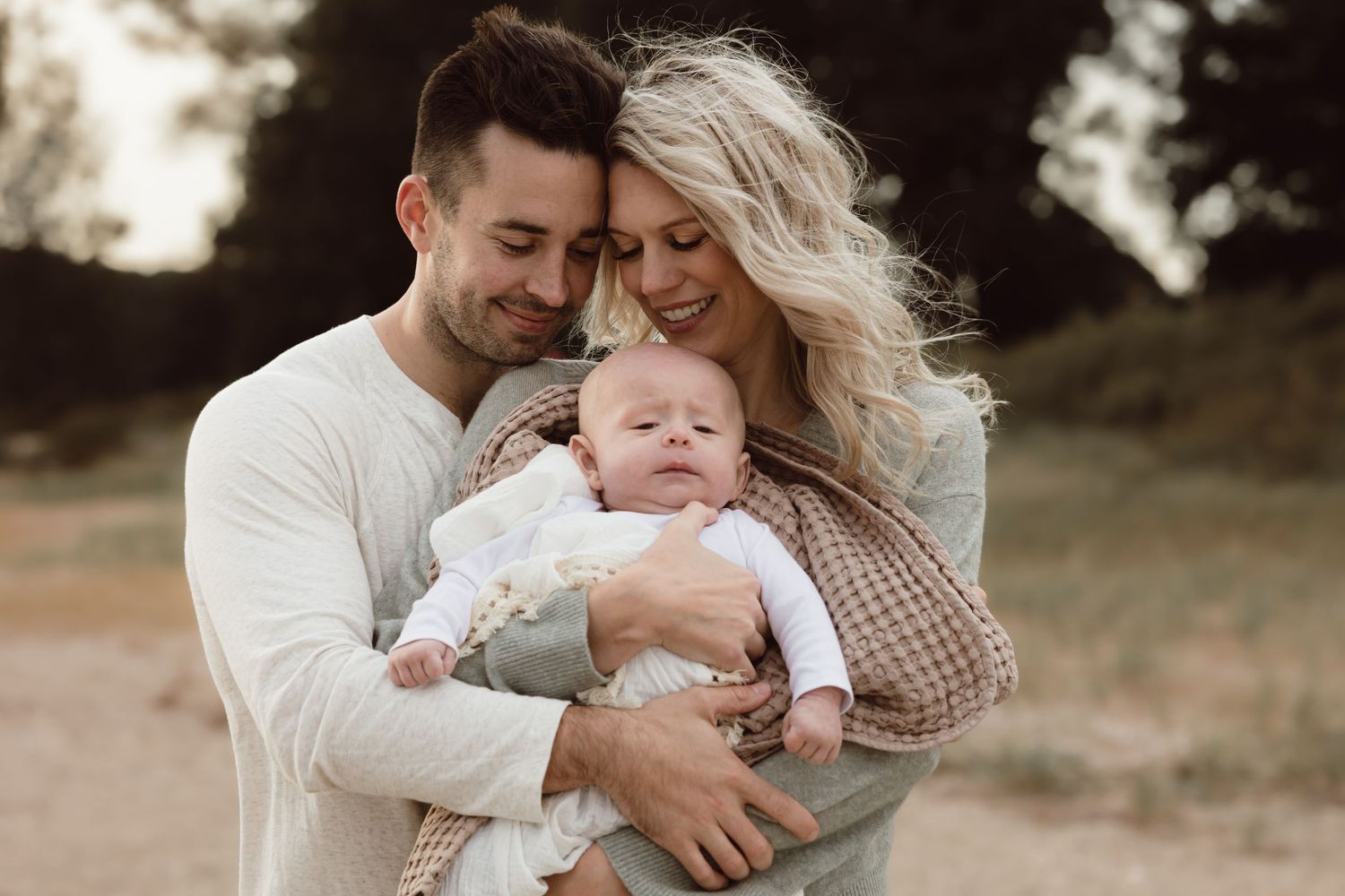 A couple embraces while holding their baby outdoors during a warm sunset photo session.