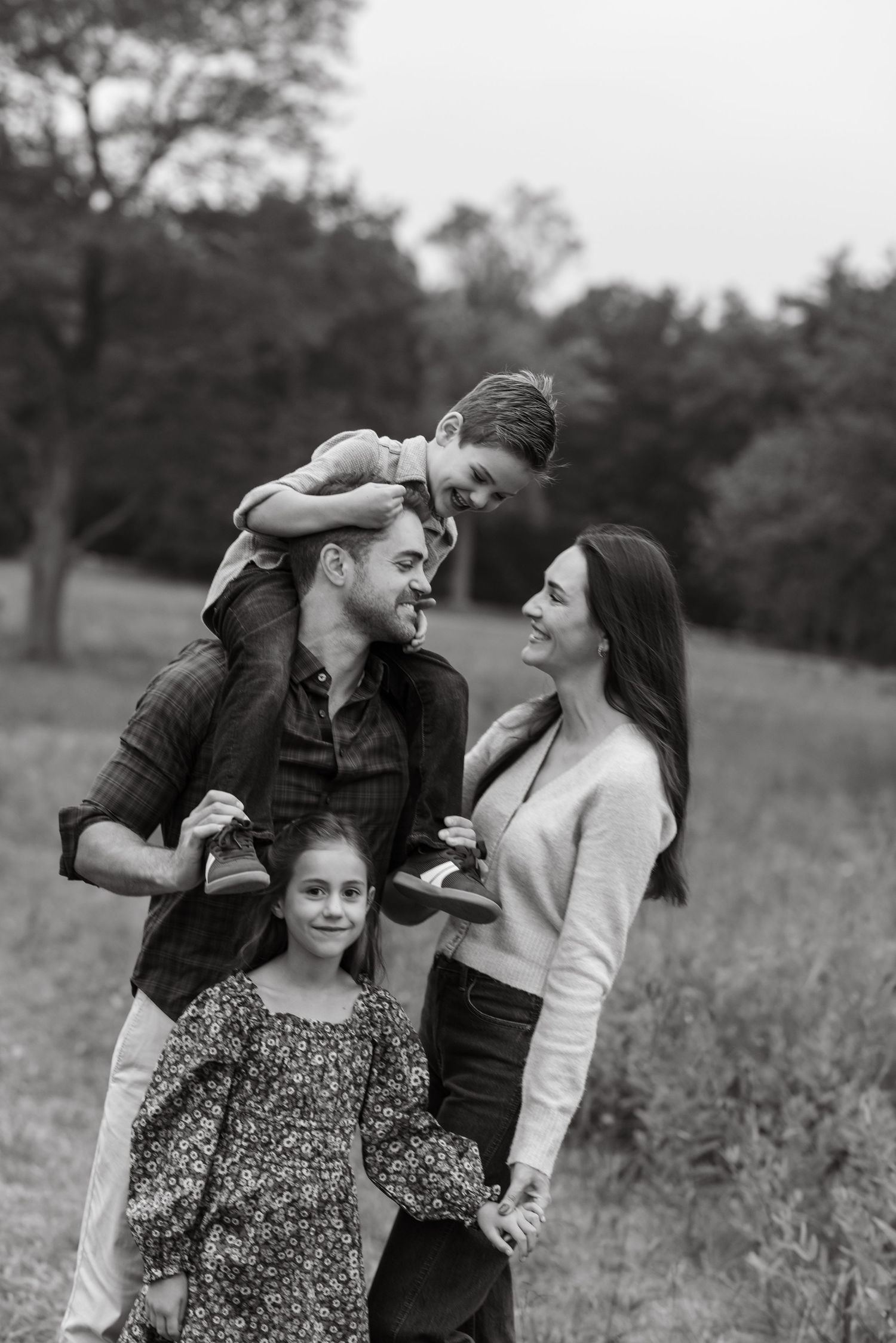 A family shares joyful moments together in a field during a black and white outdoor photo session.