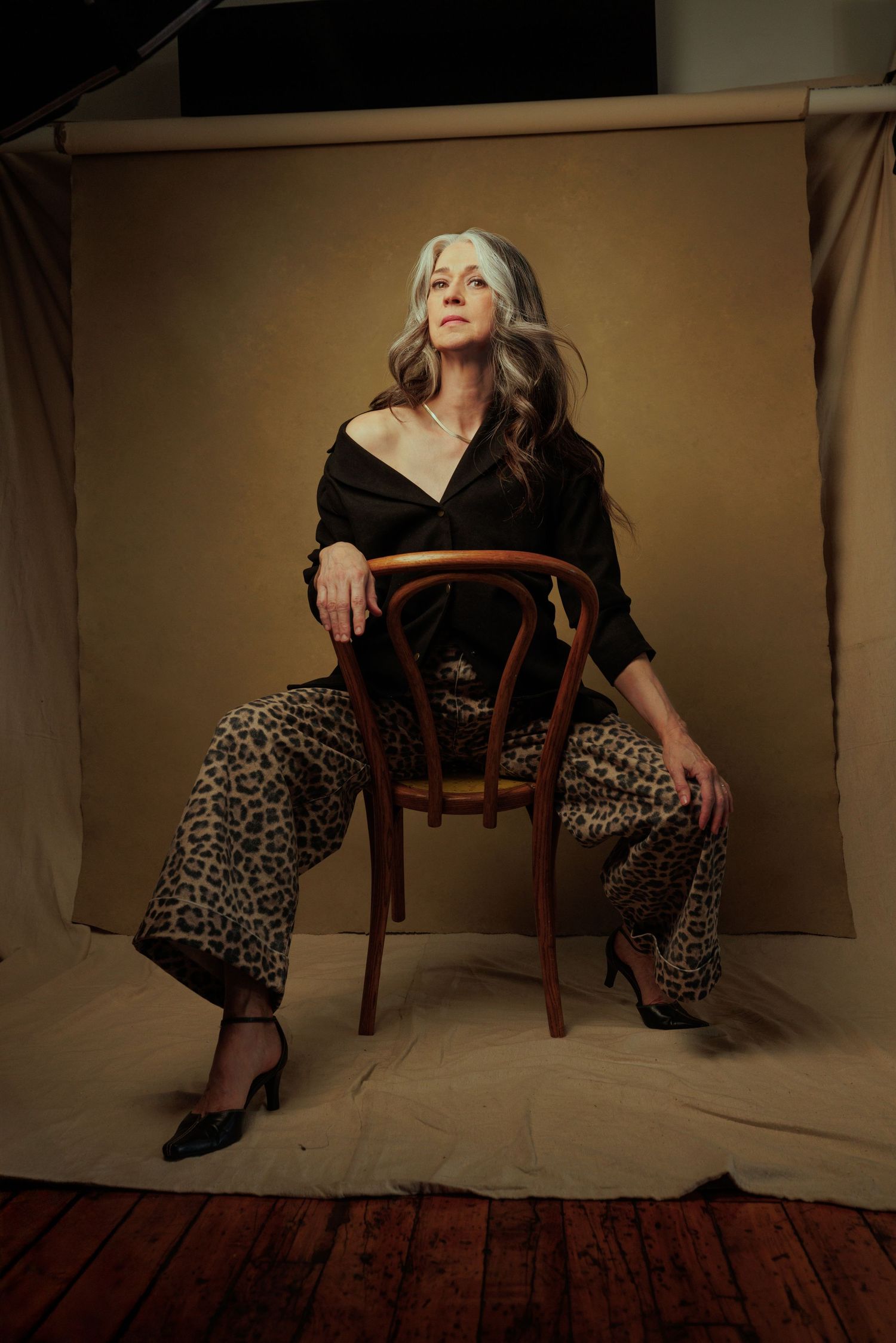 Artistic portrait series showing figure in leopard print pants posing on wooden chair against neutral backdrop for portrait photoshoot.