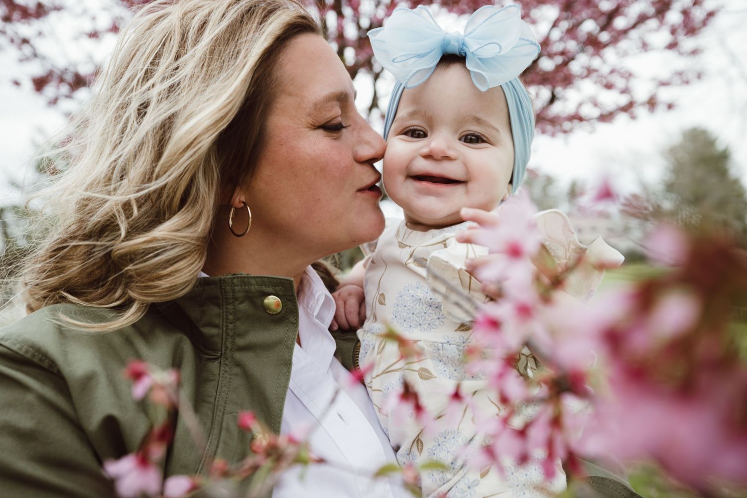 A tender moment between parent and child surrounded by blooming pink cherry blossoms on a spring day.