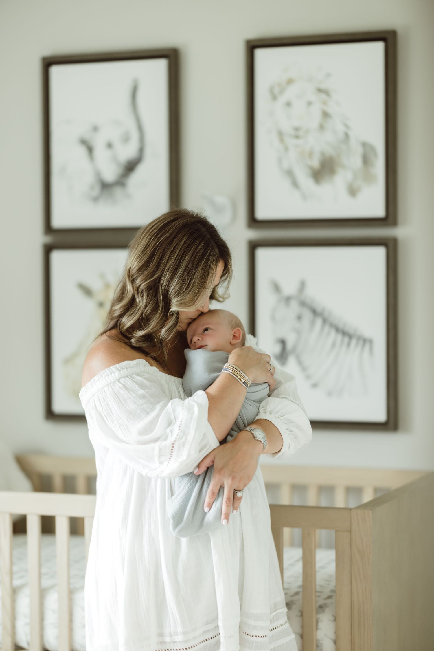 A series of four framed photos showing a person in white clothing leaning on a white crib against an animal gallery wall holding her newborn