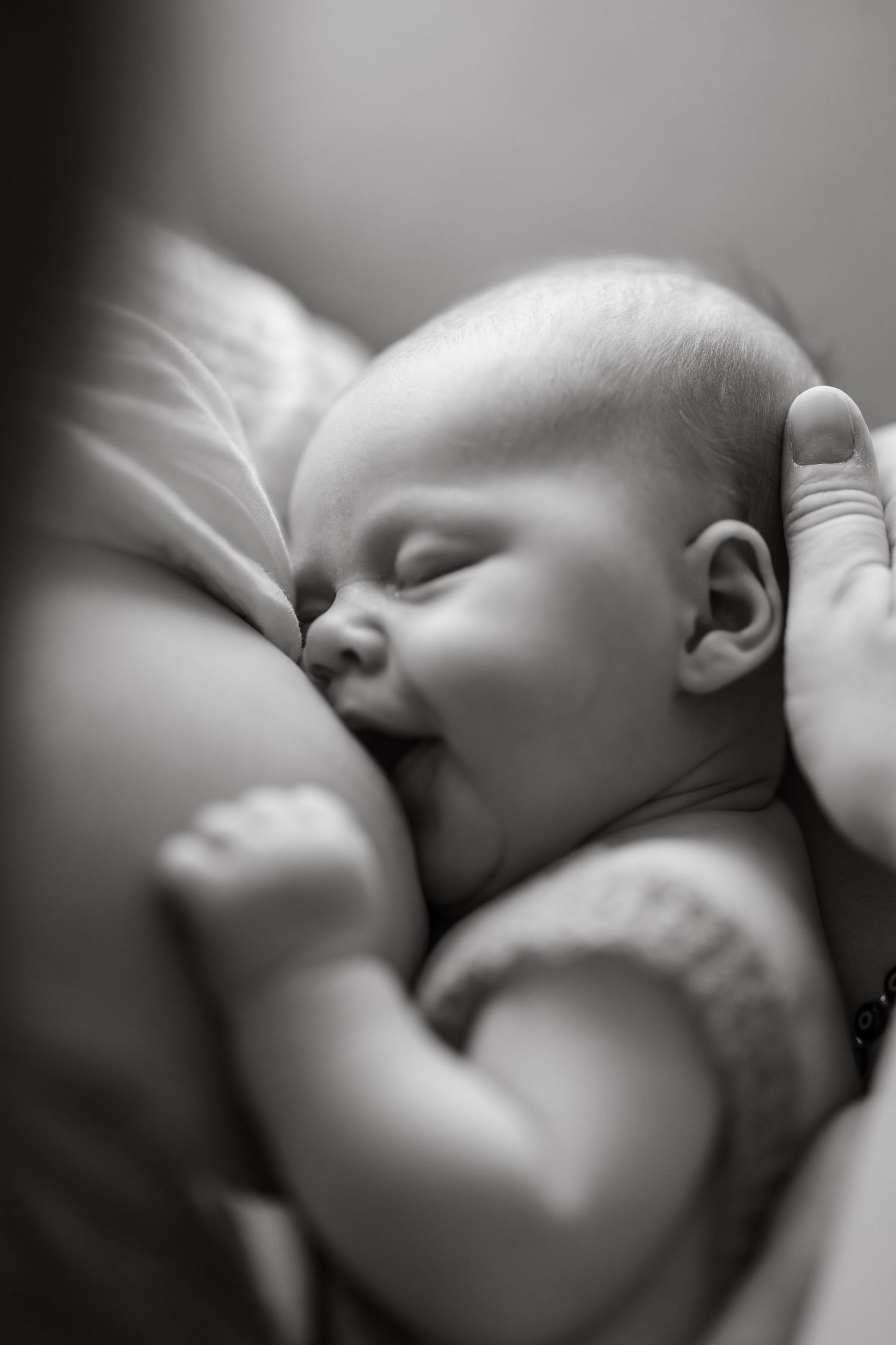 A black and white close-up image showing a baby breastfeeding in soft, intimate lighting during newborn photoshoot.