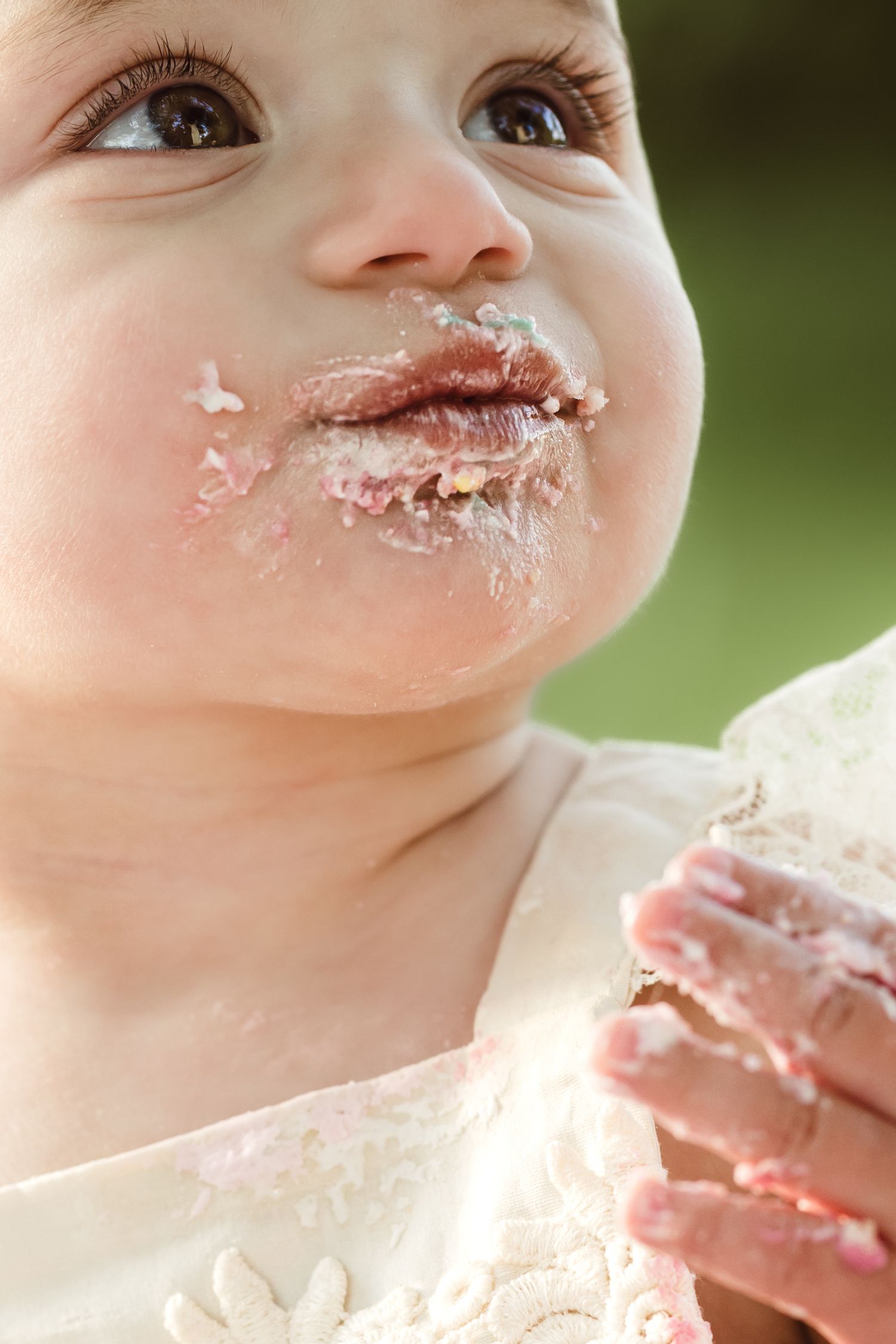 A close-up shows a baby's face and mouth covered in white frosting while enjoying their first birthday cake smash for milestone photoshoot.