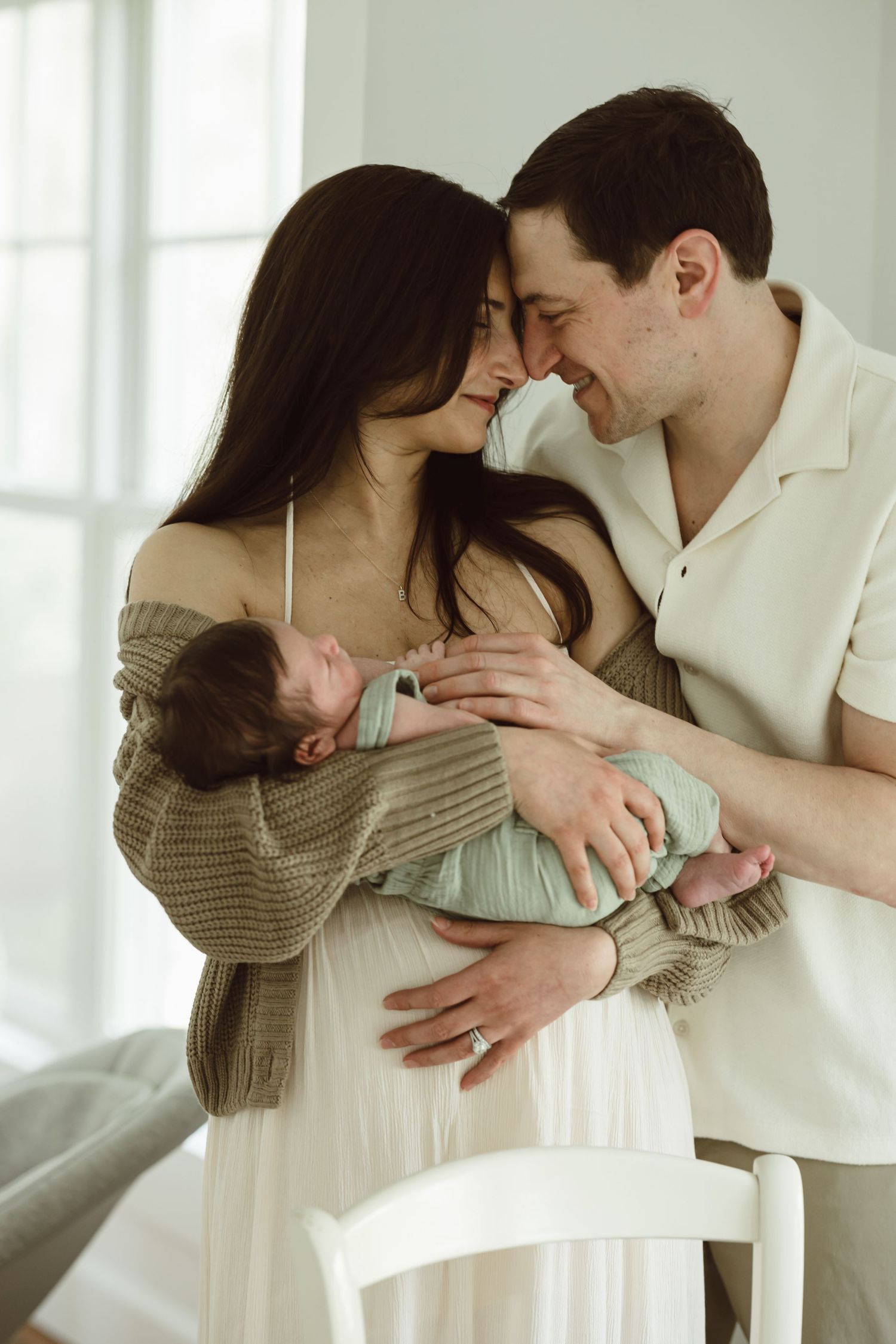 A tender family moment as parents in soft neutral clothing share an intimate moment while holding their newborn baby in kitchen in CT.