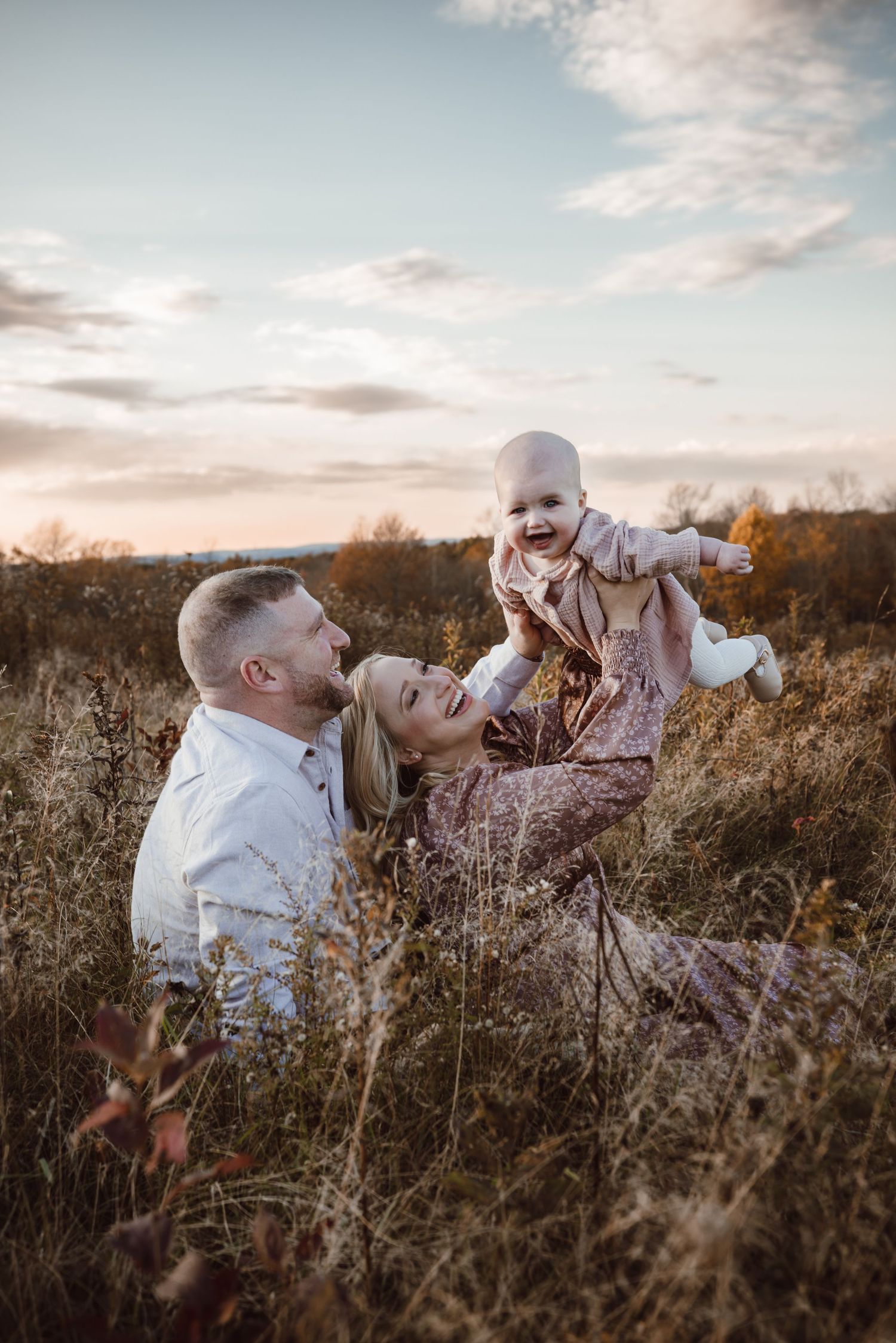 Family plays together in a golden autumn meadow at sunset as wildflowers sway in the breeze during family photoshoot.