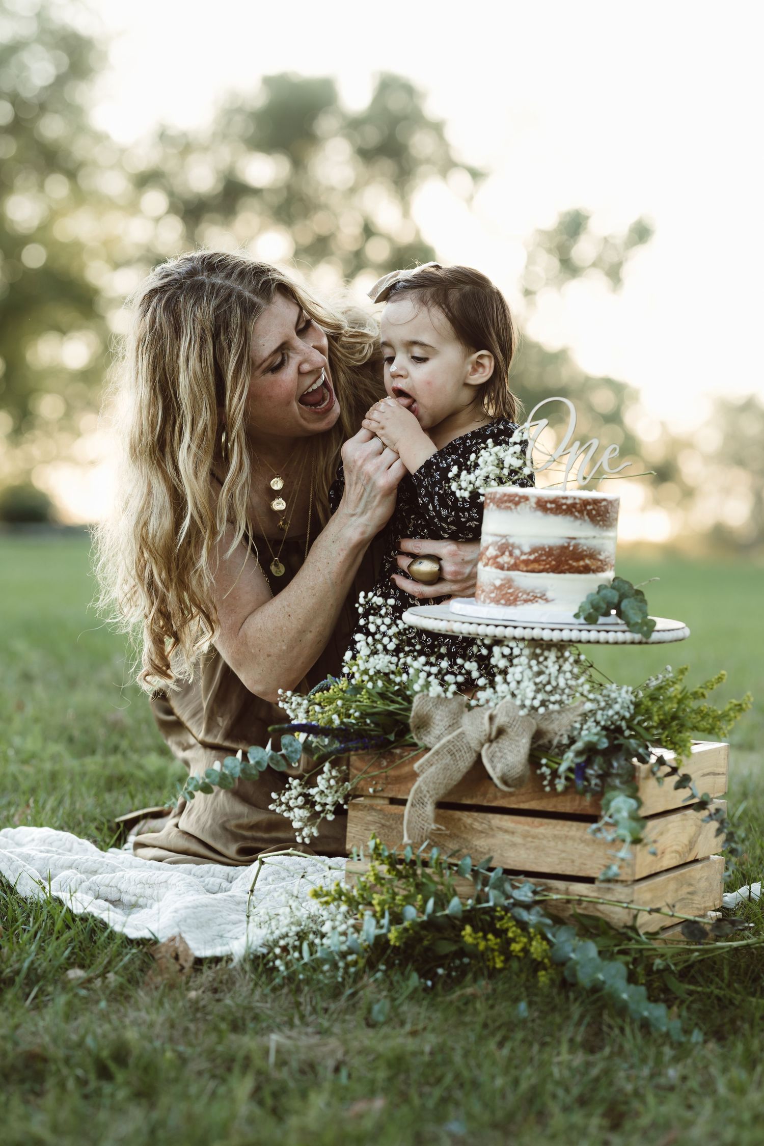 Sweet moment shared between parent and child during outdoor cake smash photo session with vintage books and flowers.