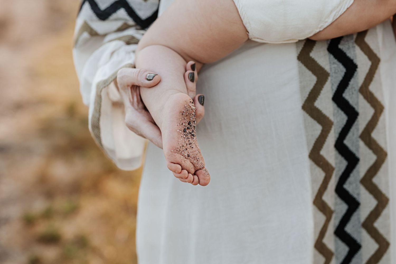 Close-up details of a one year old girls sandy foot held in her mothers hand during milestone photoshoot at CT beach.