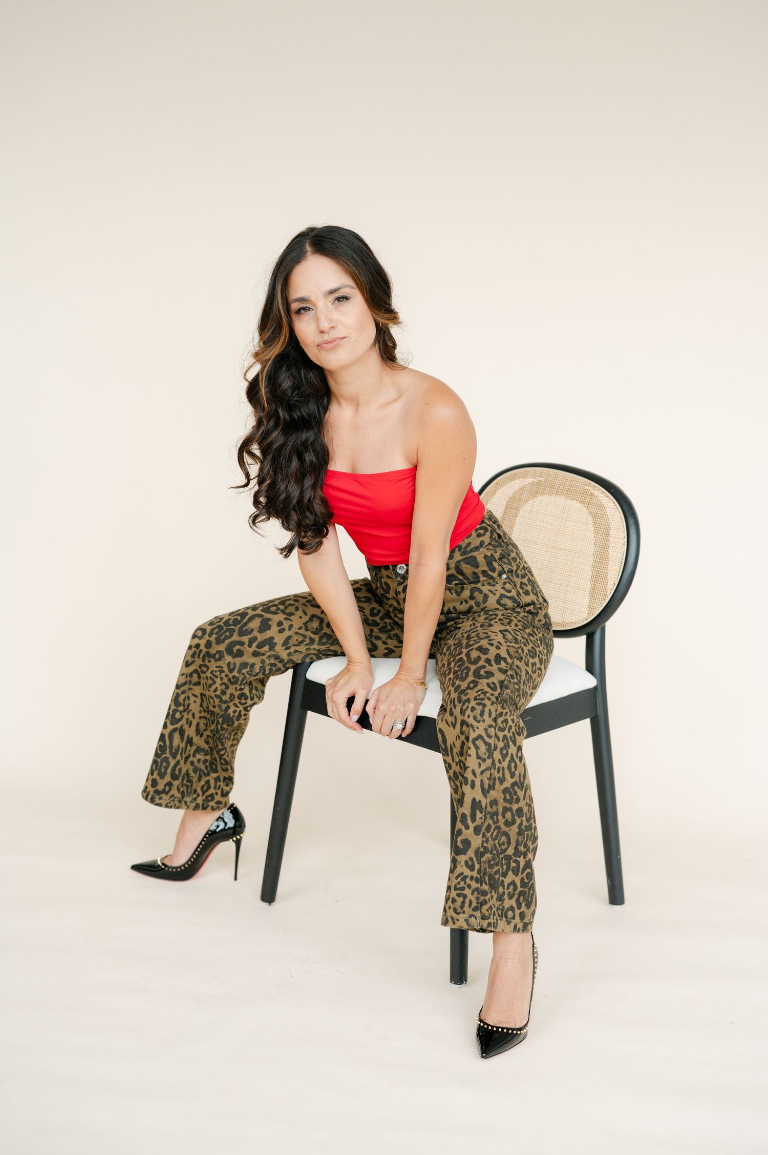 A series of fashion poses on a black chair featuring leopard print pants and a red top against a white backdrop.