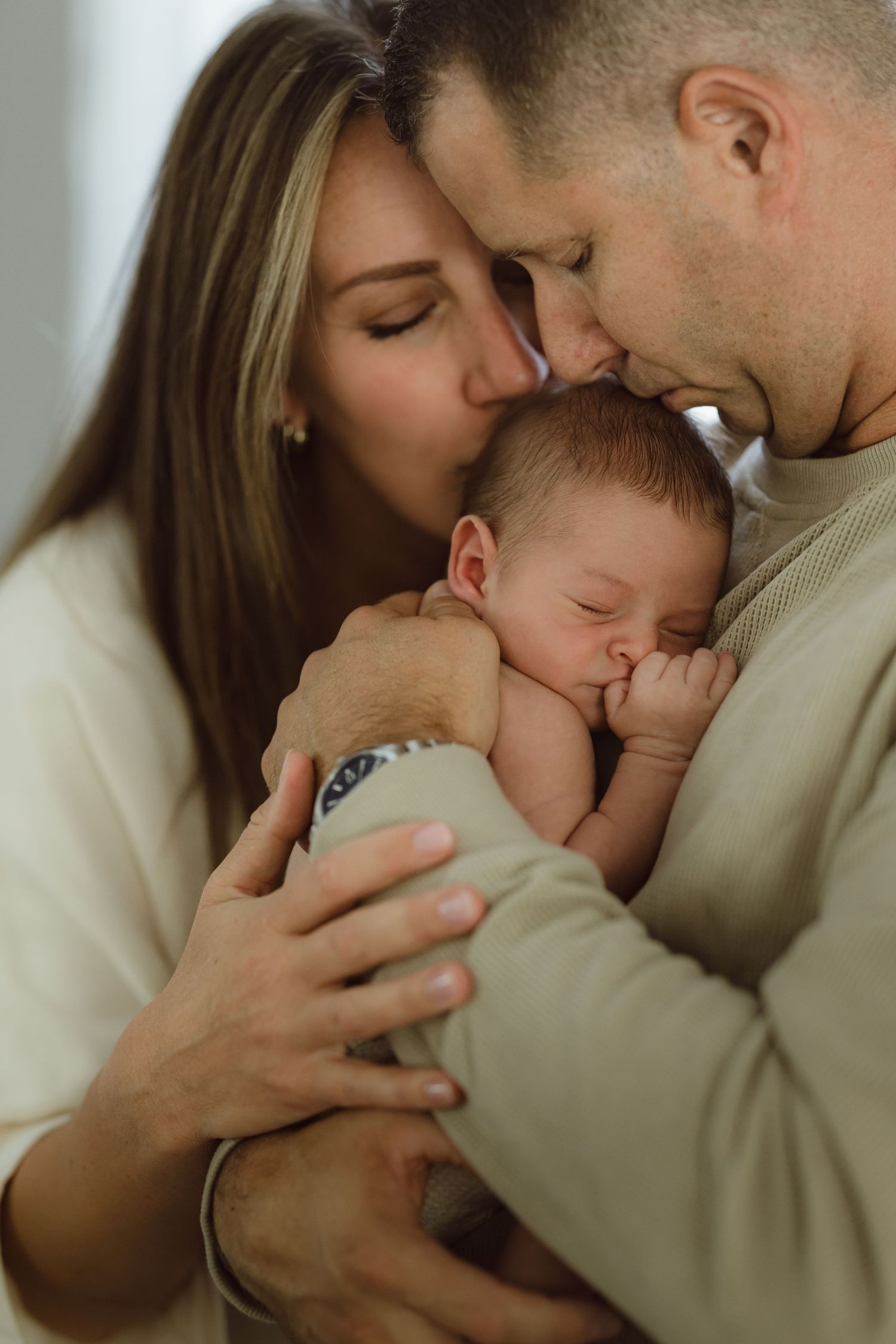 Mother and Father holding each other and their newborn baby while kissing him on his head with their eyes closed.