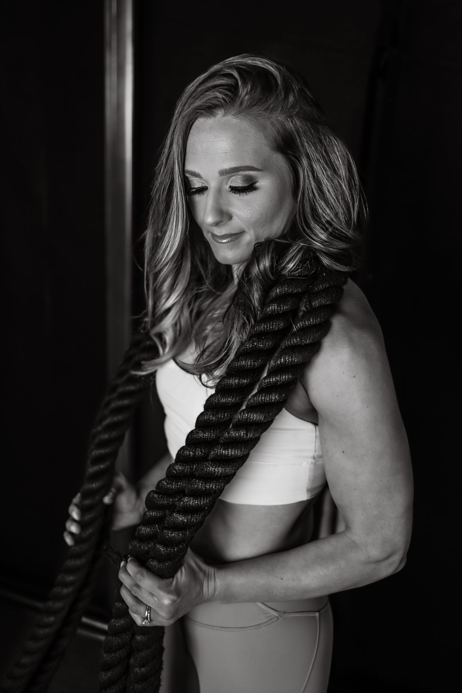 Athletic woman in workout attire holds battle ropes during strength training session in black and white photo.