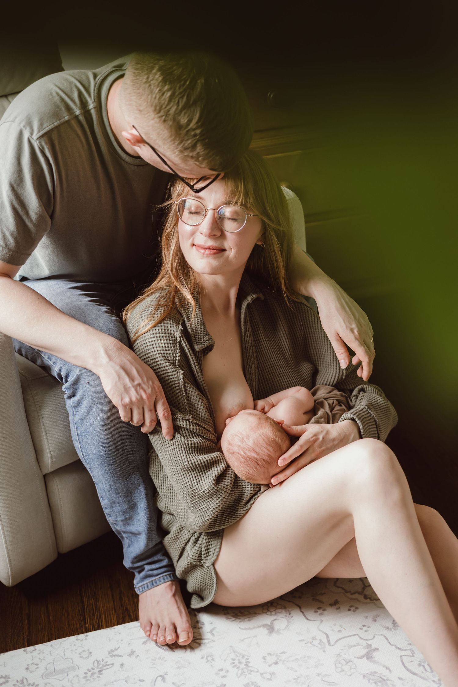 Intimate lifestyle photo series showing tender moments of first time parents. Mother breastfeeding and husband kissing her forefead.