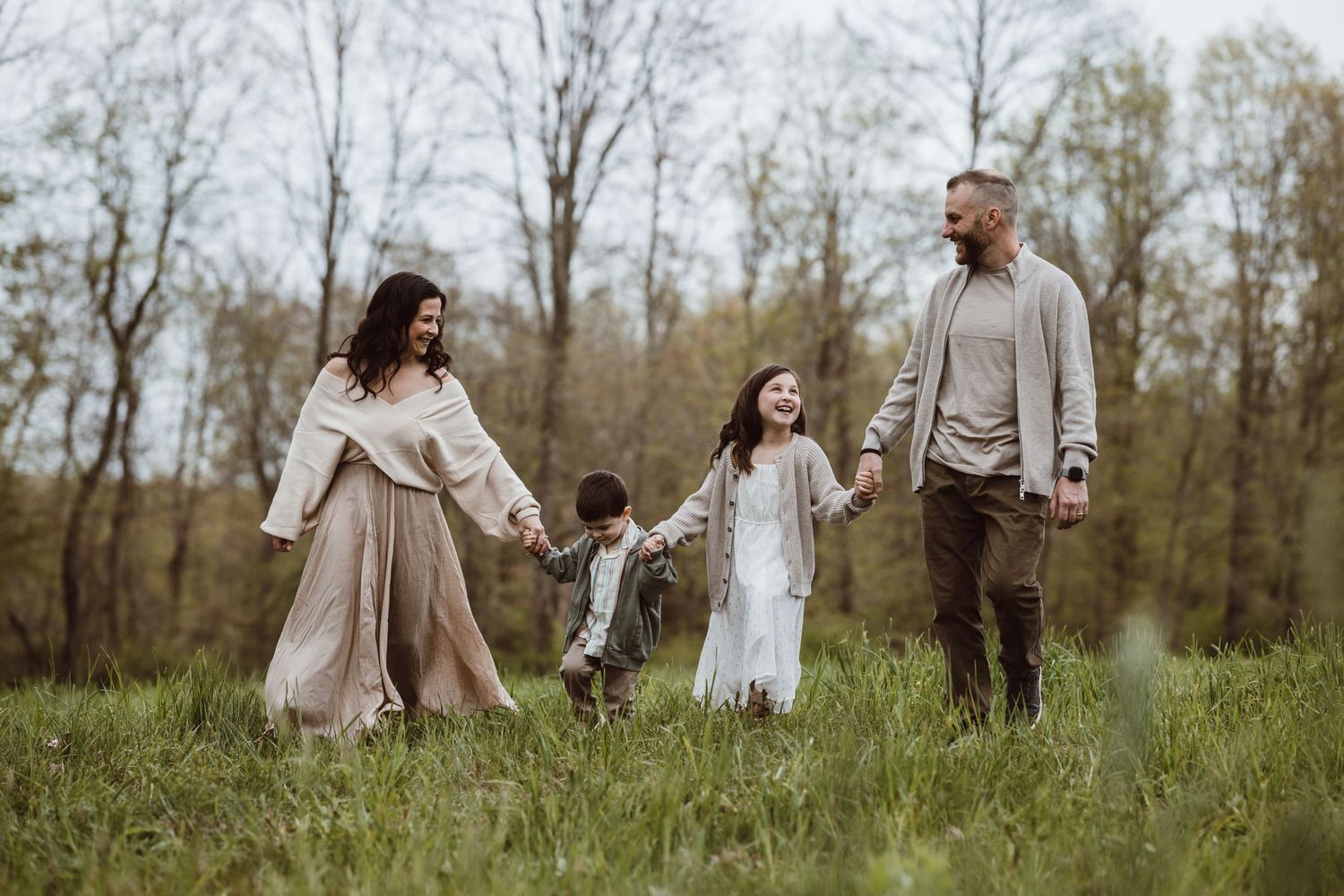 Family holding hands while walking through a serene meadow on an autumn afternoon.