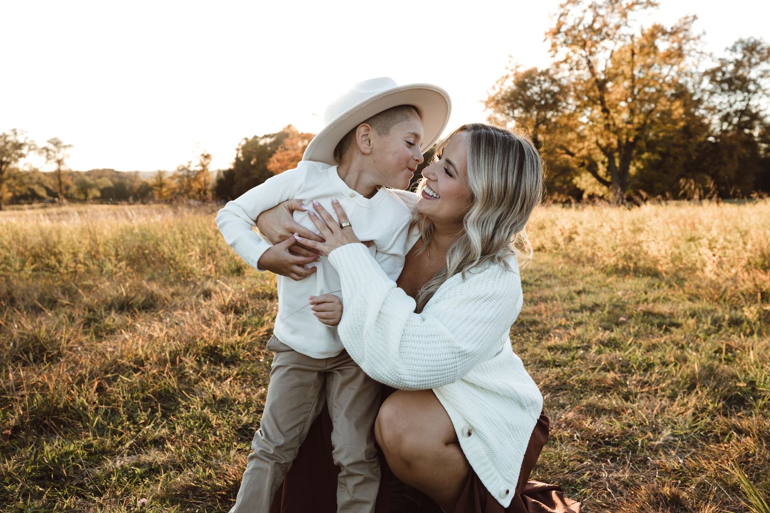 A mother and son shares tender moments in a sunlit field during golden hour as they pose for romantic outdoor photos.