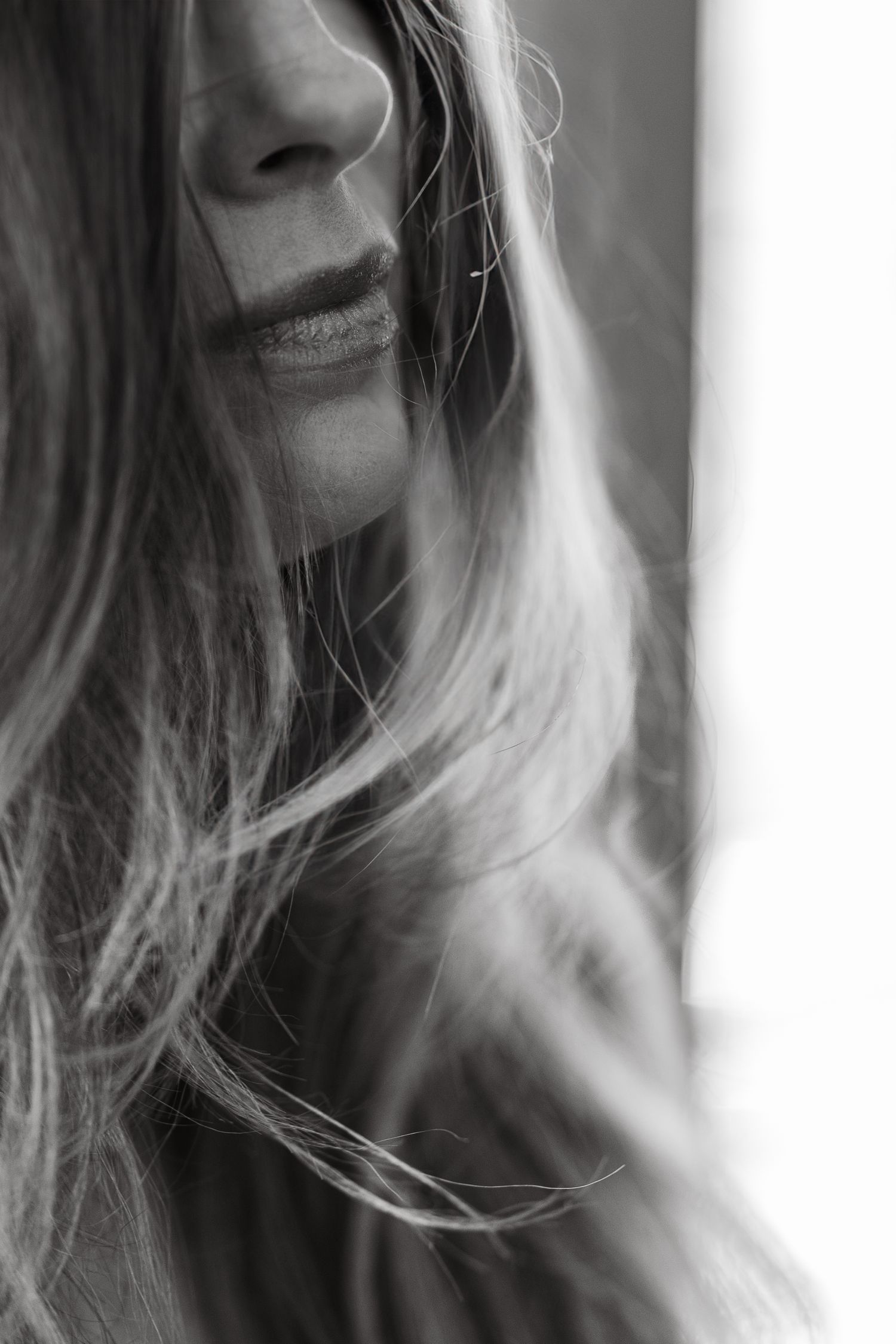 Black and white artistic portrait showing a woman's smile and flowing hair in soft focus for boudoir photoshoot.