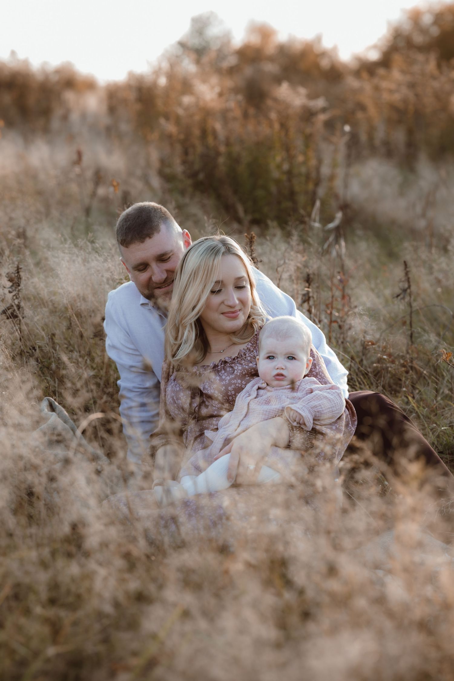 Family sharing tender moments together in a golden autumn field during sunset in Connecticut for milestone photoshoot.